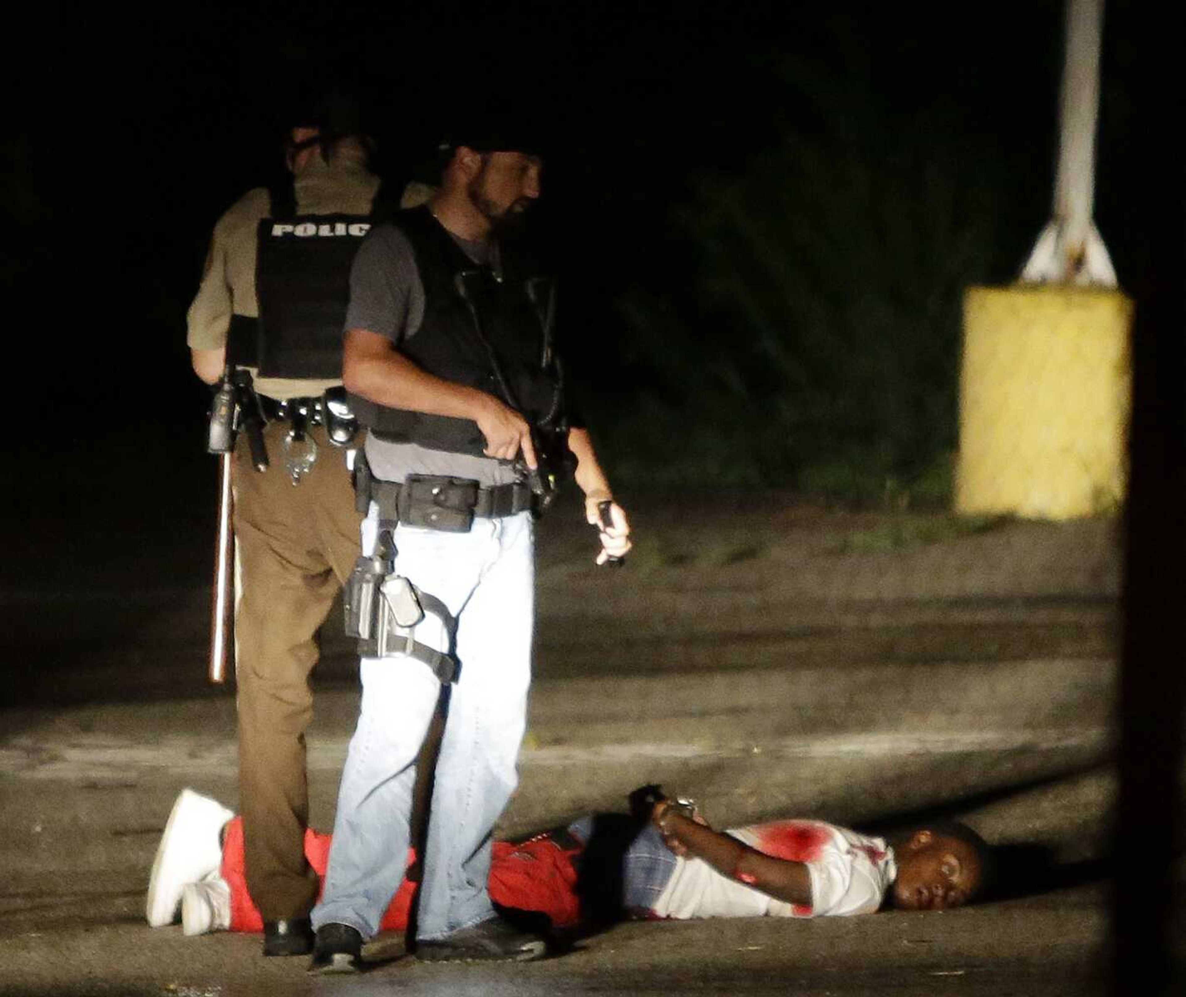 Police stand near suspect Tyrone Harris Jr. in a parking lot Aug. 9 after gunfire during a protest on the anniversary of the death of Michael Brown in Ferguson, Missouri. Harris is accused of shooting at undercover officers with a gun stolen from Cape Girardeau. (Jeff Roberson ~ Associated Press)