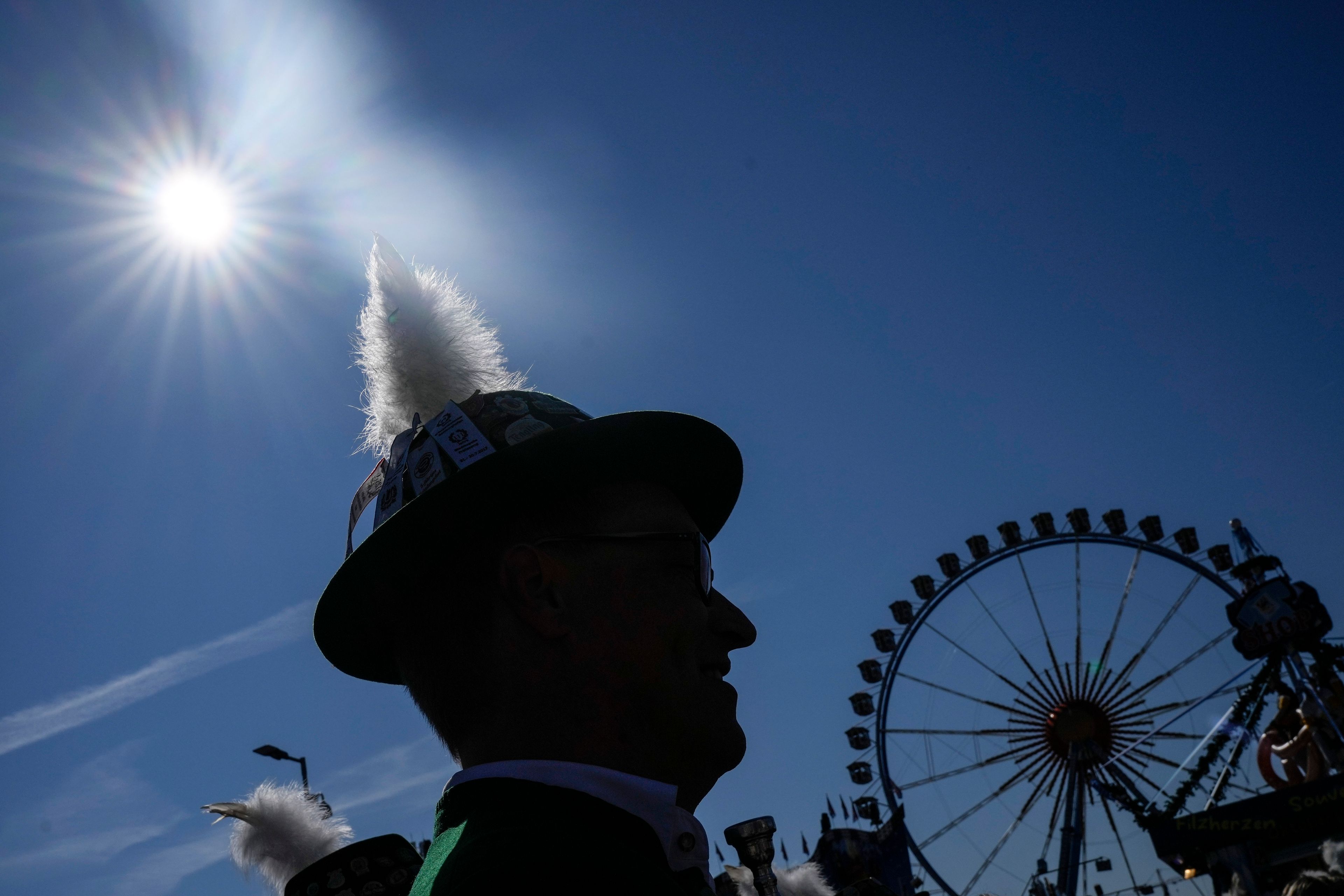 A man with a traditional Bavarian hat is pictured at the start of the 189th 'Oktoberfest' beer festival in front of paintings showing Munich landmarks in Munich, Germany, Saturday, Sept. 21, 2024. (AP Photo/Matthias Schrader)