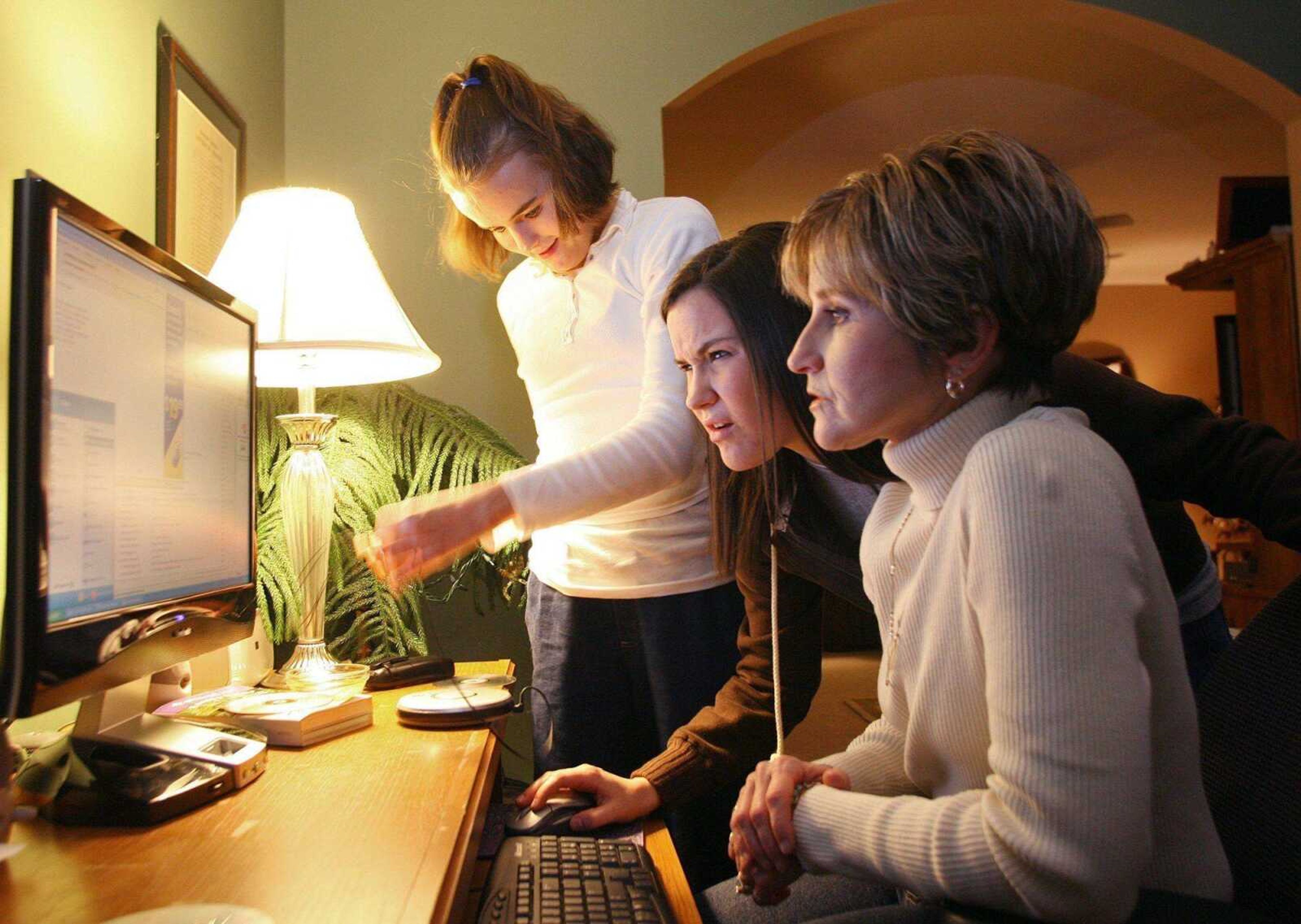 Molly Cantonwine, left, 16, her sister Sara Cantonwine, 18, and their mother, St. Louis Public Schools superintendent Diana Bourisaw, looked for e-mailed photos Dec. 20 at their home in south St. Louis County. (Christian Gooden ~ St. Louis Post-Dispatch)