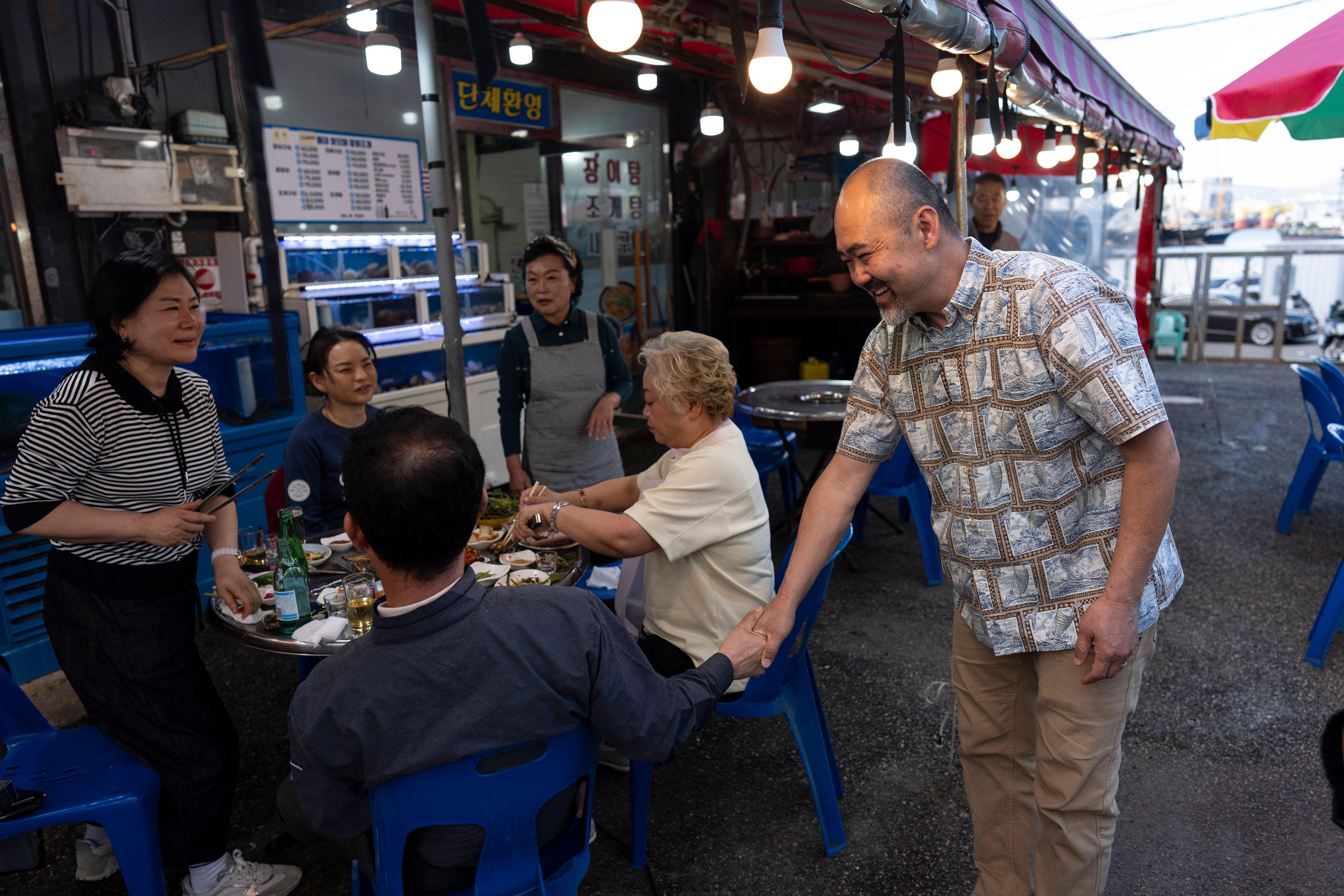 Kenneth Barthel, right, who was adopted to the United States at 6 years old, talks with diners in the neighborhood where he remembers being abandoned by his mother, in Busan, South Korea, Friday, May 17, 2024. Barthel was posting flyers in the area featuring his photos in the hopes of finding his birth family. (AP Photo/Jae C. Hong)