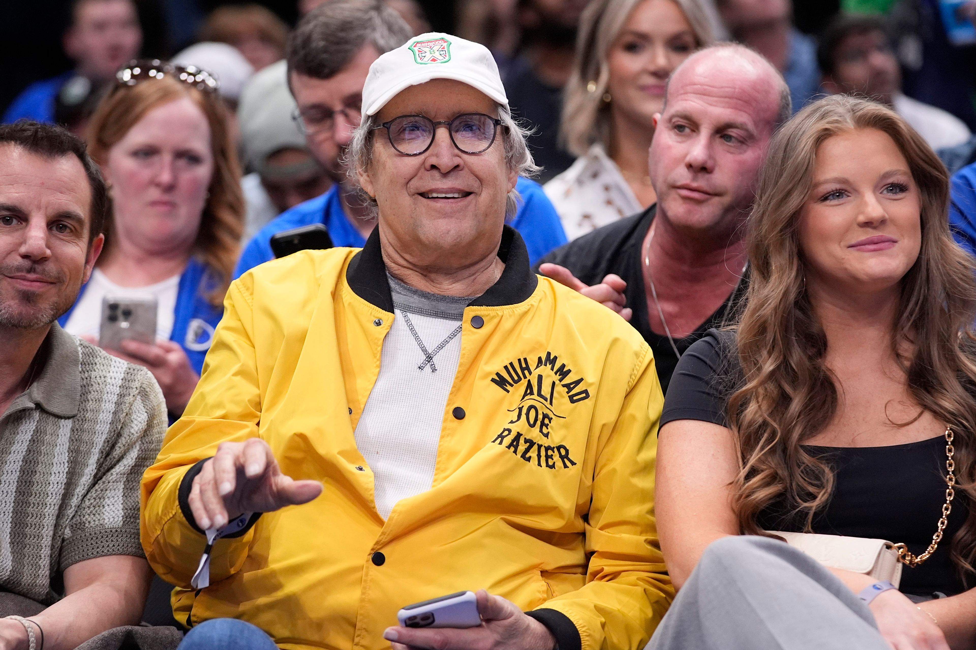 FILE - Actor Chevy Chase, center, sits on the front row during the second half of an NBA basketball game between the Atlanta Hawks and Dallas Mavericks in Dallas on April 4, 2024. (AP Photo/LM Otero, File)