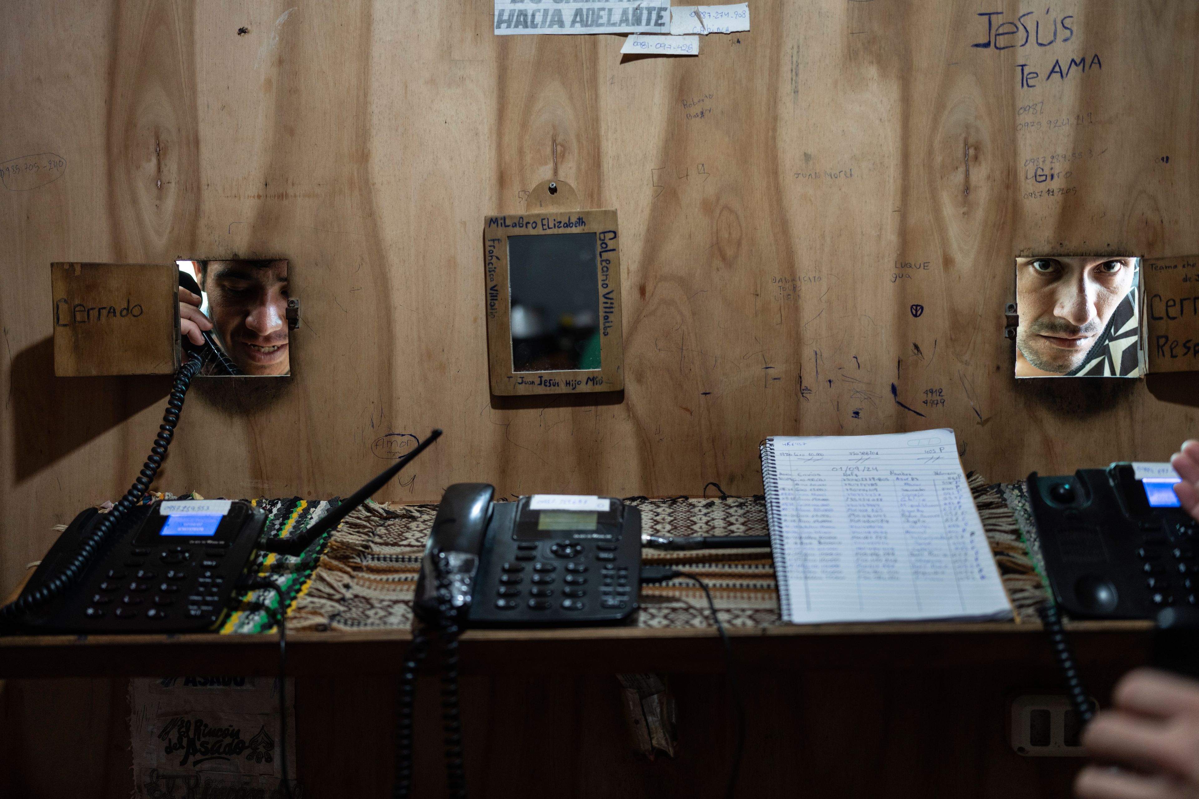 An inmate uses a phone as another gives the number to dial at a pay-by-the-minute phone booth set up and run by prisoners at the Regional Penitentiary in Villarica, Paraguay, Sunday, Sept. 1, 2024. Most inmates' calls get paid for by their families when they come to visit in person. (AP Photo/Rodrigo Abd)