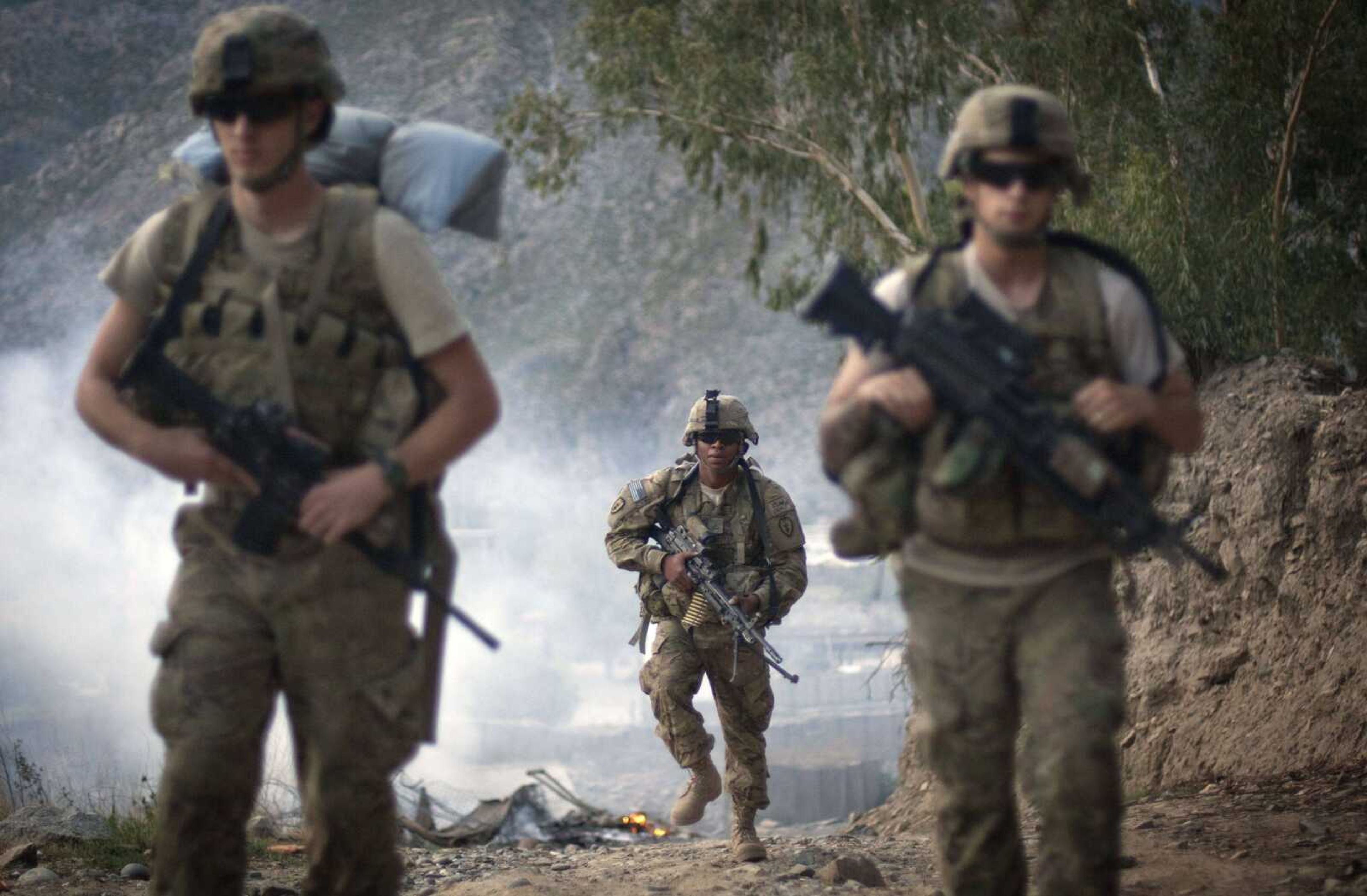 U.S. Army Pfc. Garrick Carlton, center, of Sacramento, California, hikes past burning rubbish to man a hilltop observation post along with fellow Pfc. Michael Tompkins, of Wadsworth, Ohio, left, and Pfc. Austin D'Amica, of San Diego, at Combat Outpost Monti in September 2011 in Kunar province, Afghanistan. (AP Photo/David Goldman, File)