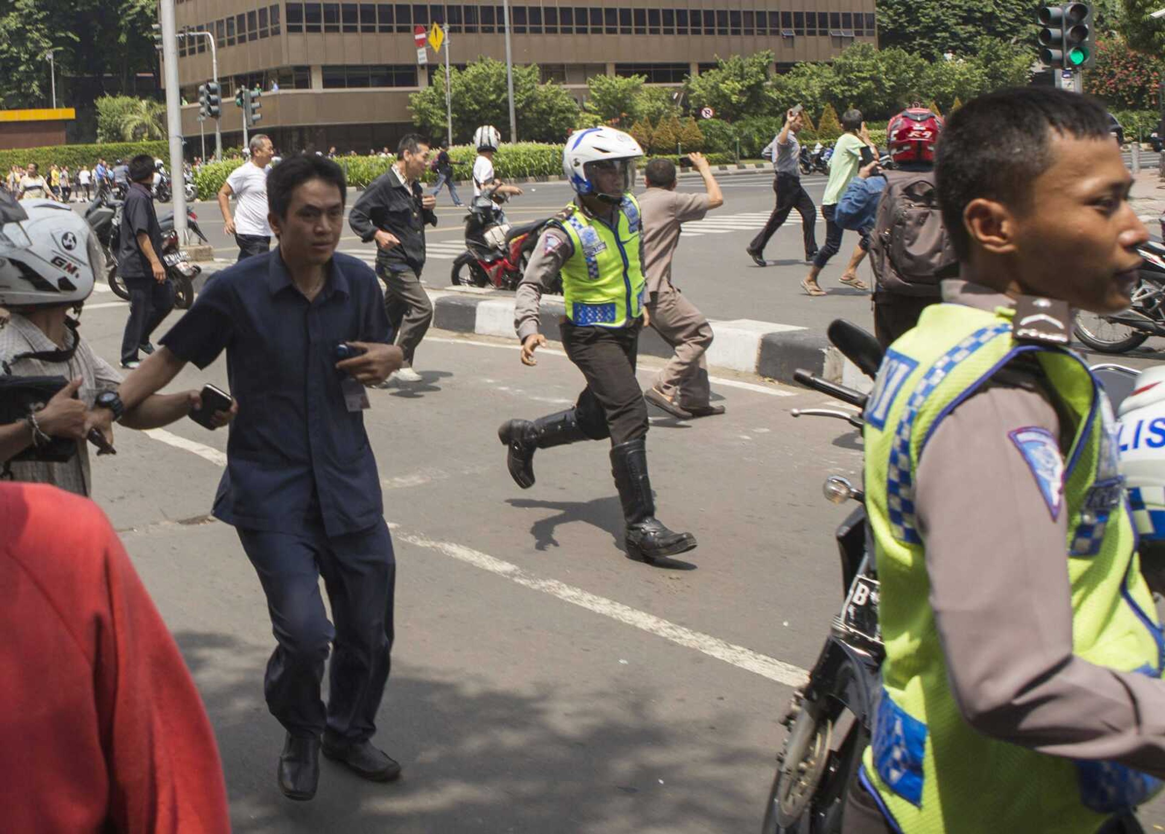 People, including unarmed police officers, flee from the scene after a gun battle broke out Thursday following an explosion in Jakarta, Indonesia. (Associated Press)