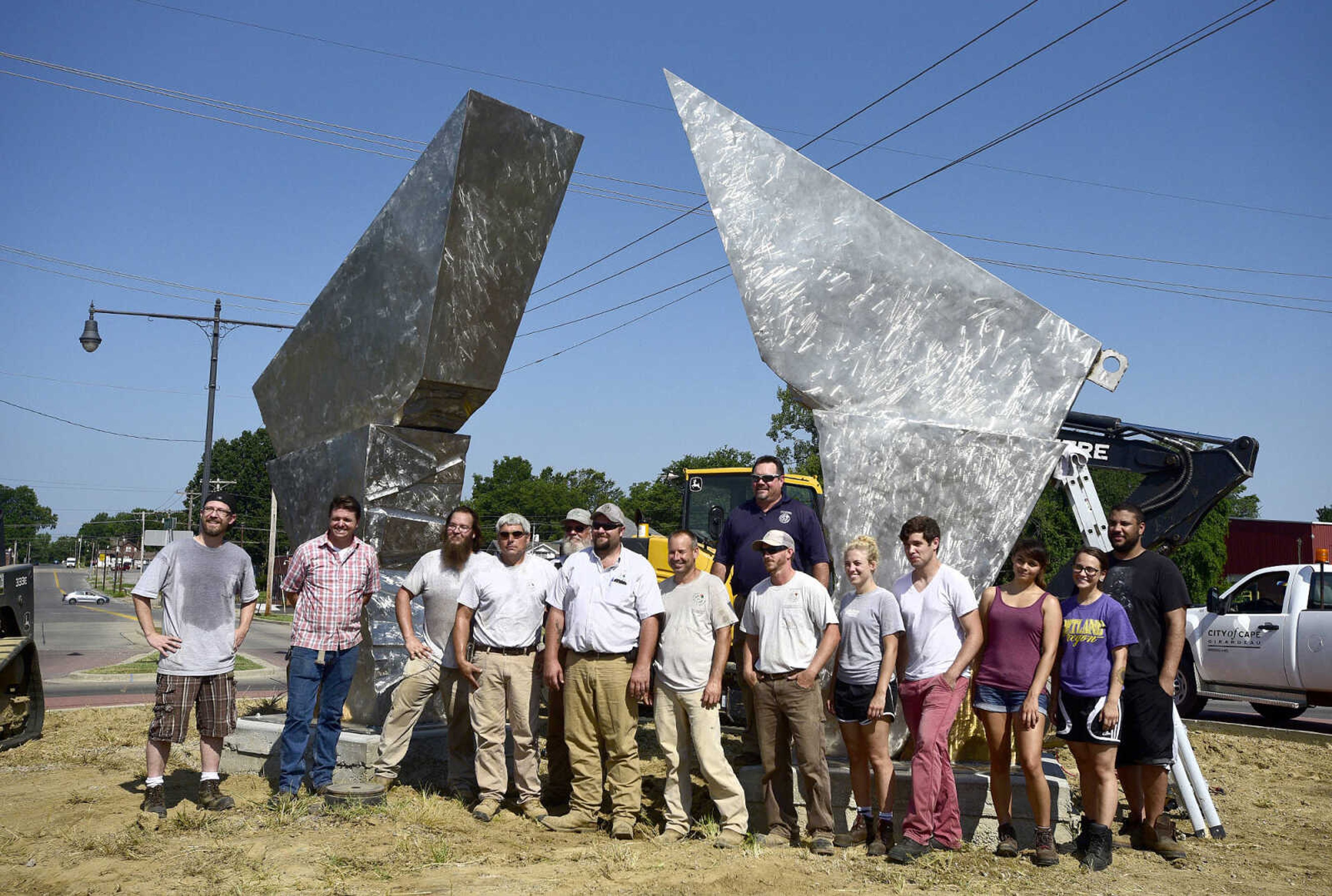 Chris Wubbena, left, Cape Girardeau Parks and Recreation Department employees, and current and former Southest Missouri State University students pose for a photo after the installation of Wubbena's 14-foot sculpture, "Commence", in the Fountain Street roundabout on Monday, July 24, 2017, near the River Campus. The students helped build the sculpture.