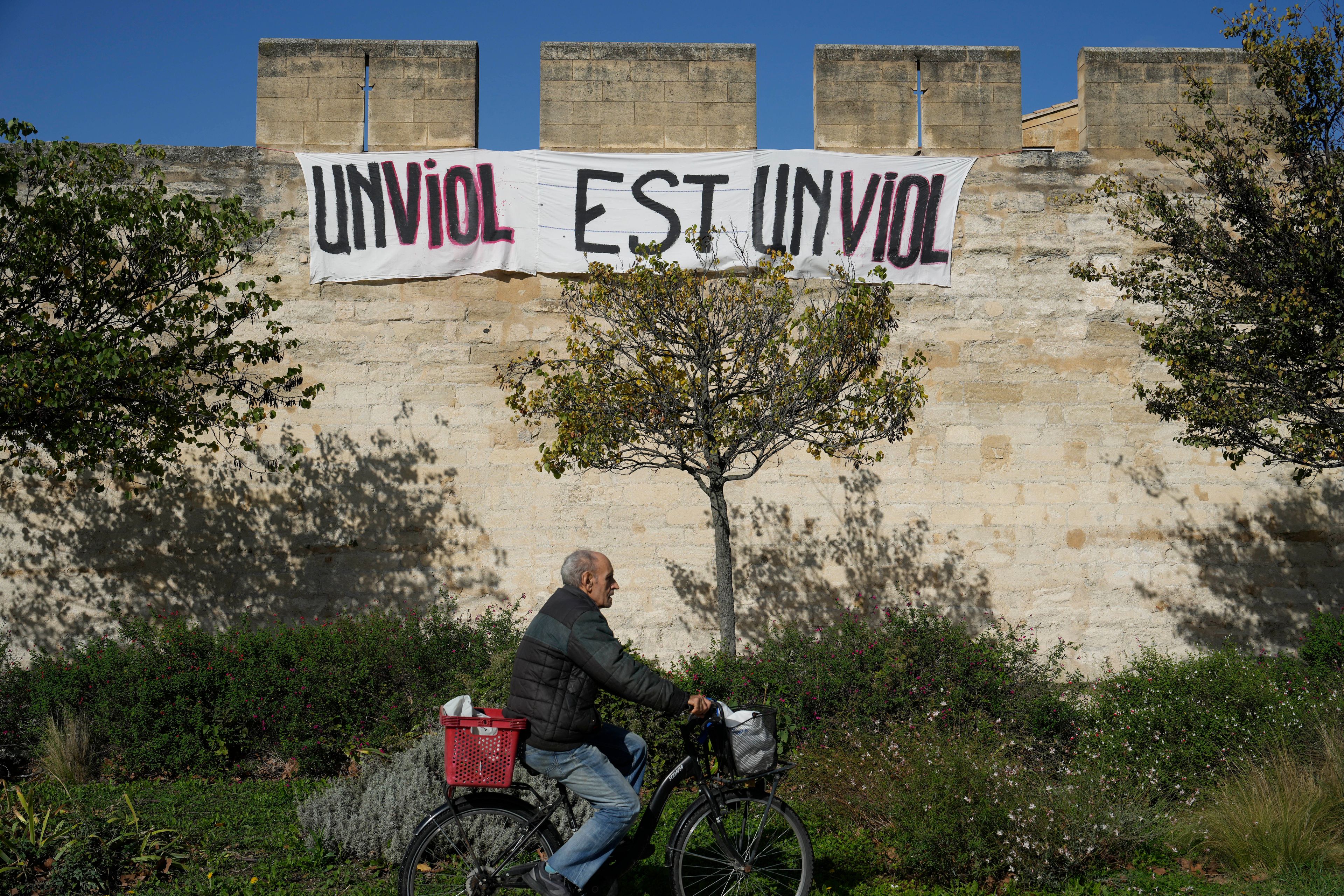 A man rides a bicycle in front of a banner reading: "A rape is a rape," in Avignon, southern France, Wednesday, Oct. 16, 2024. (AP Photo/Lewis Joly)