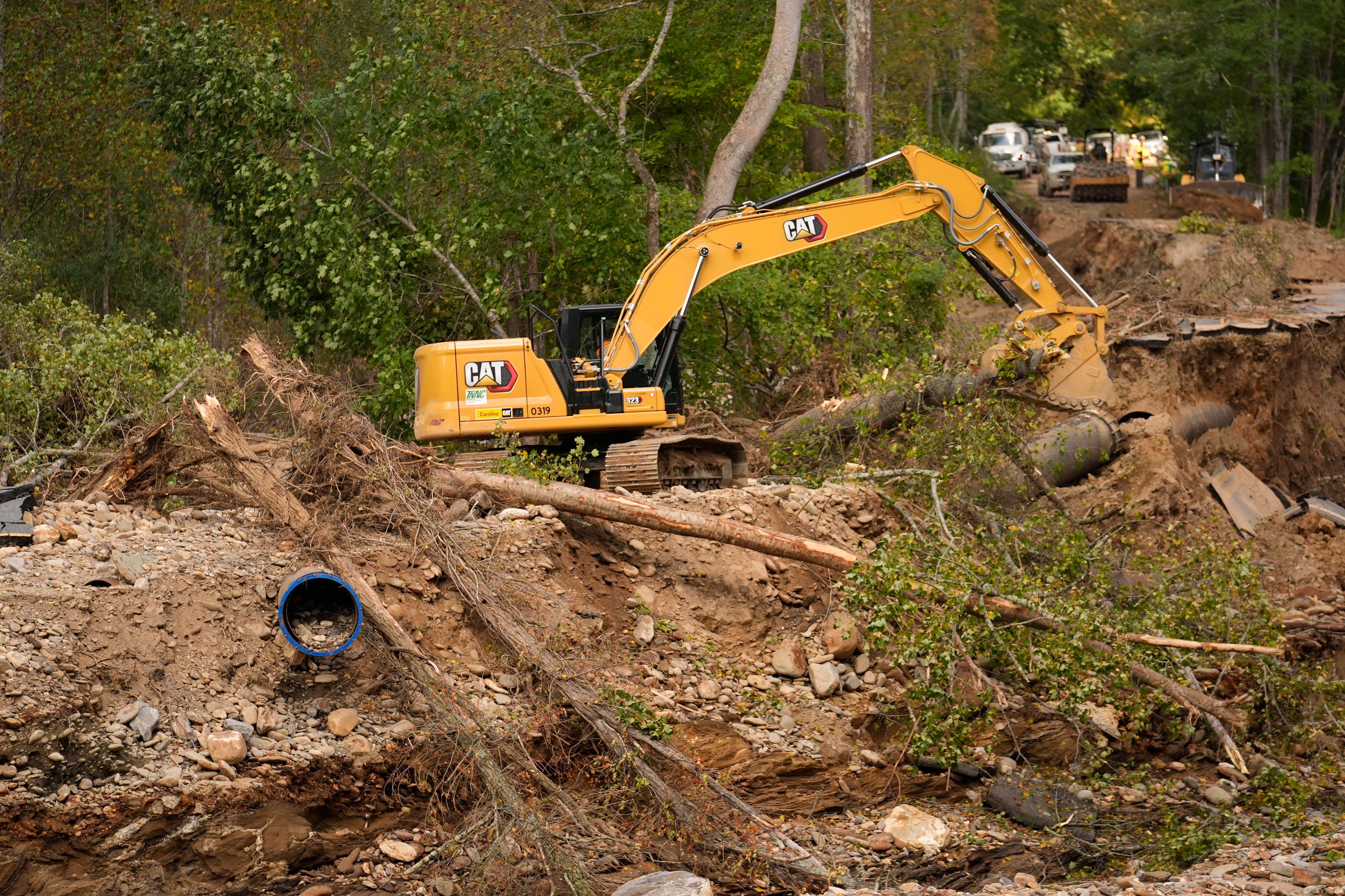 A backhoe is used to clear debris left by Hurricane Helene that washed away a road and destroyed a waterline for the city of Asheville Wednesday, Oct. 2, 2024, in Black Mountain, N.C. (AP Photo/Jeff Roberson)