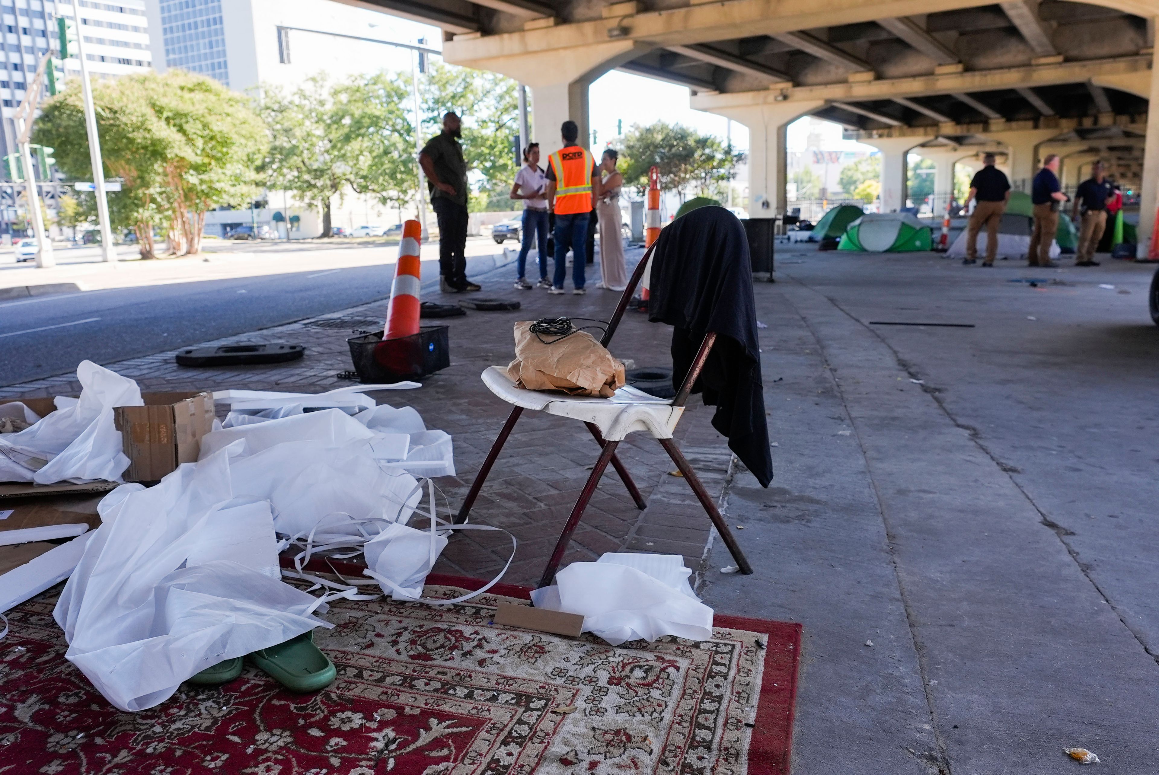 Possessions sit under an overpass as Louisiana State police, right, give instructions to people living in a homeless encampment to move to a different pre-designated location as they perform a sweep in advance of a Taylor Swift concert in New Orleans, Wednesday, Oct. 23, 2024. (AP Photo/Gerald Herbert)