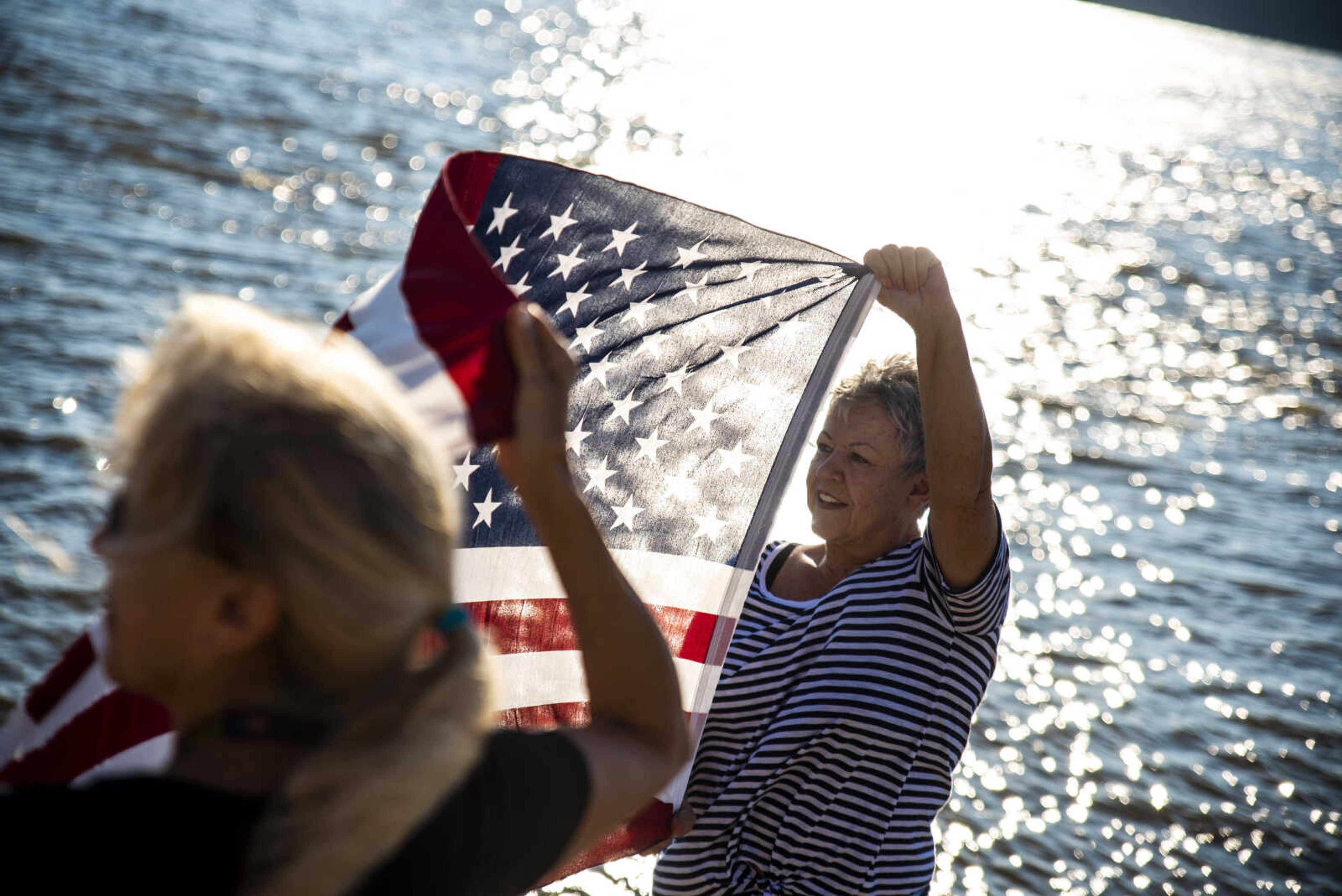 Sue Kemp, right, and Dale Humphries, left, hold up an American flag as Rick Baine, Ryan Webb and Matt Roy (none pictured) approach the Cape Girardeau Riverfront during their Warrior Paddle Expedition from source to sea of the Mississippi River Tuesday, Aug. 28, 2018 in Cape Girardeau.