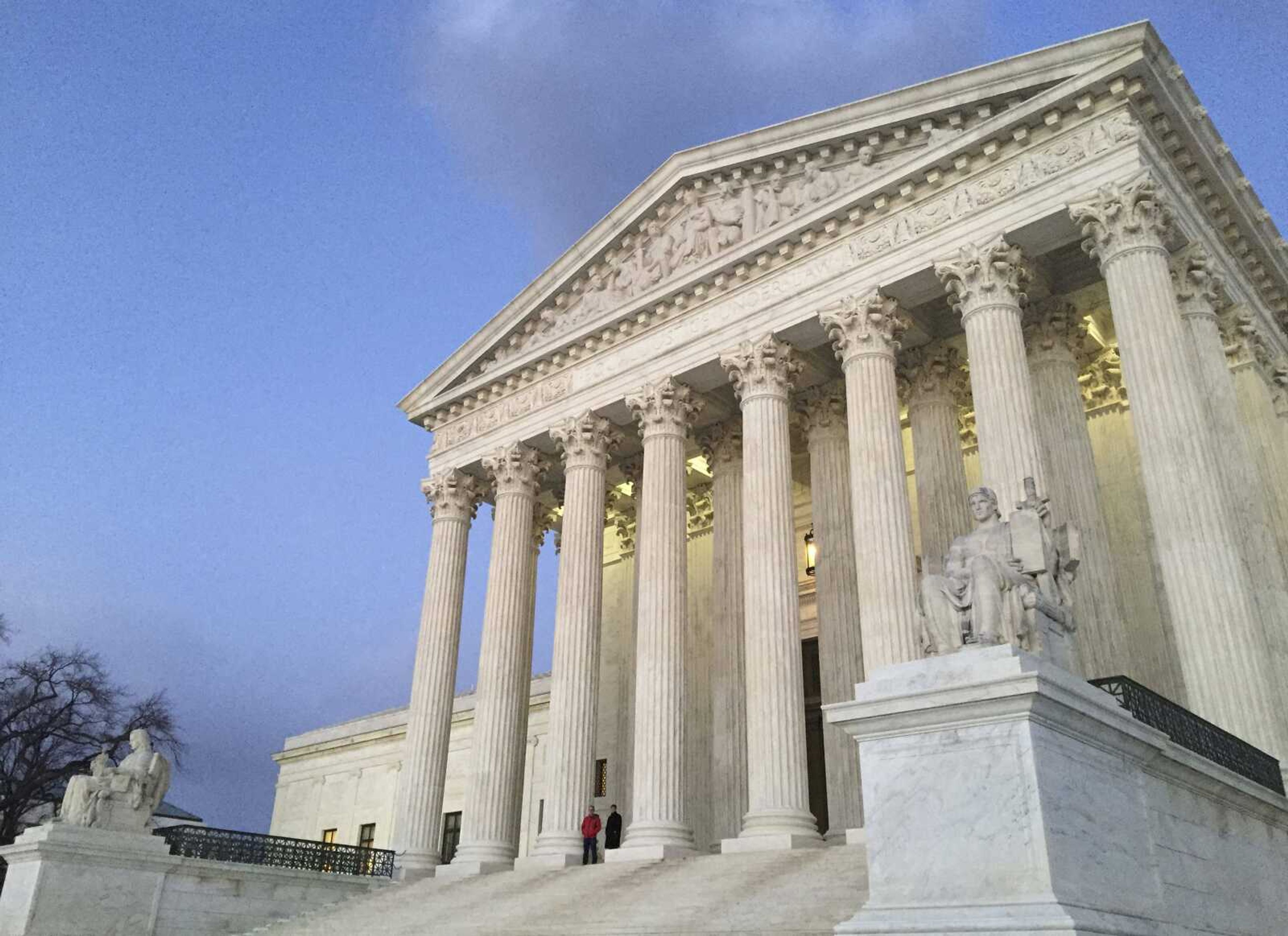 People stand on the steps of the U.S. Supreme Court at sunset in Washington.