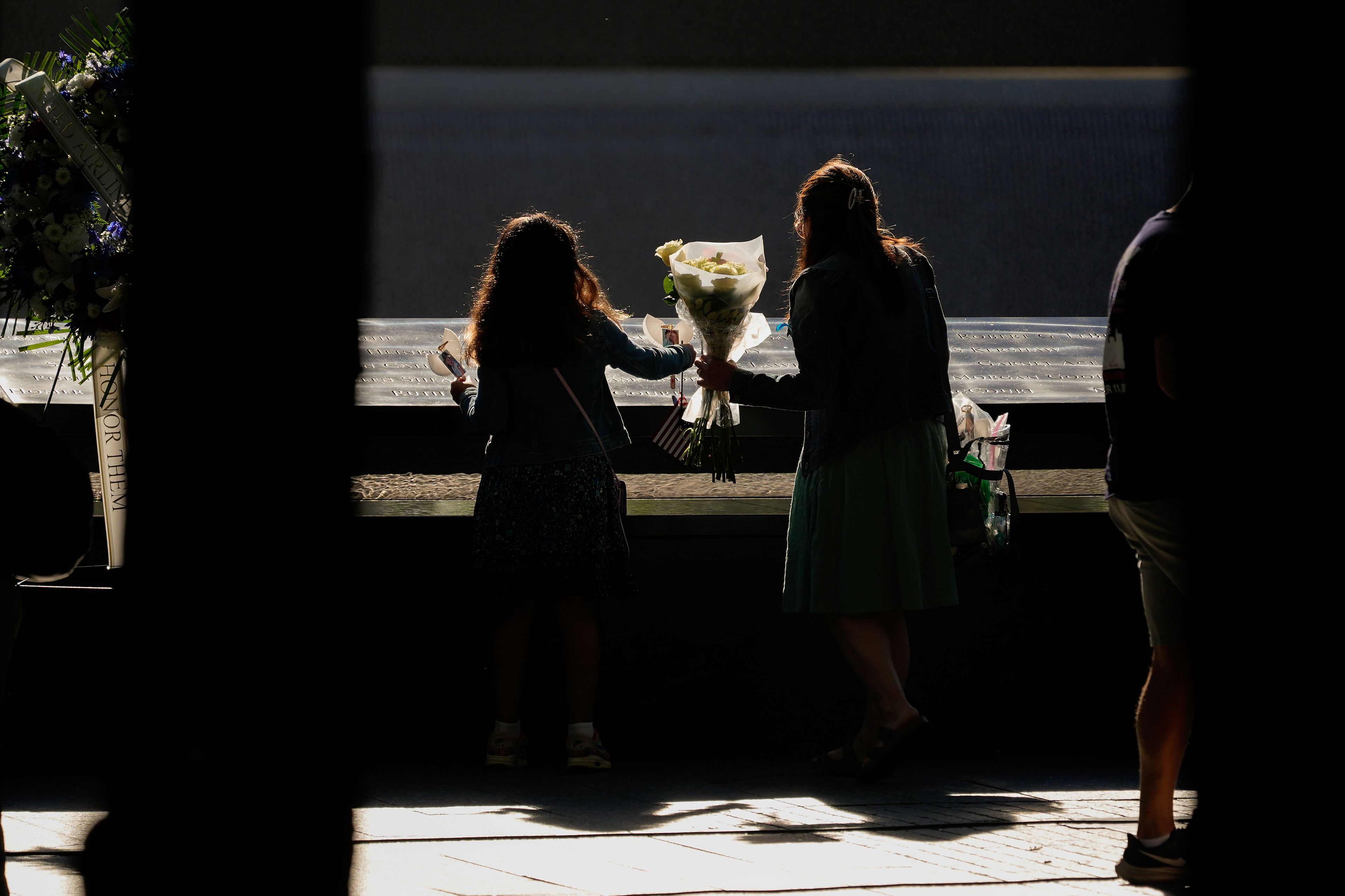 People place flowers on the bronze parapets that ring the reflecting pools during the 9/11 Memorial ceremony on the 23rd anniversary of the Sept. 11, 2001 attacks, Wednesday, Sept. 11, 2024, in New York. (AP Photo/Pamela Smith)