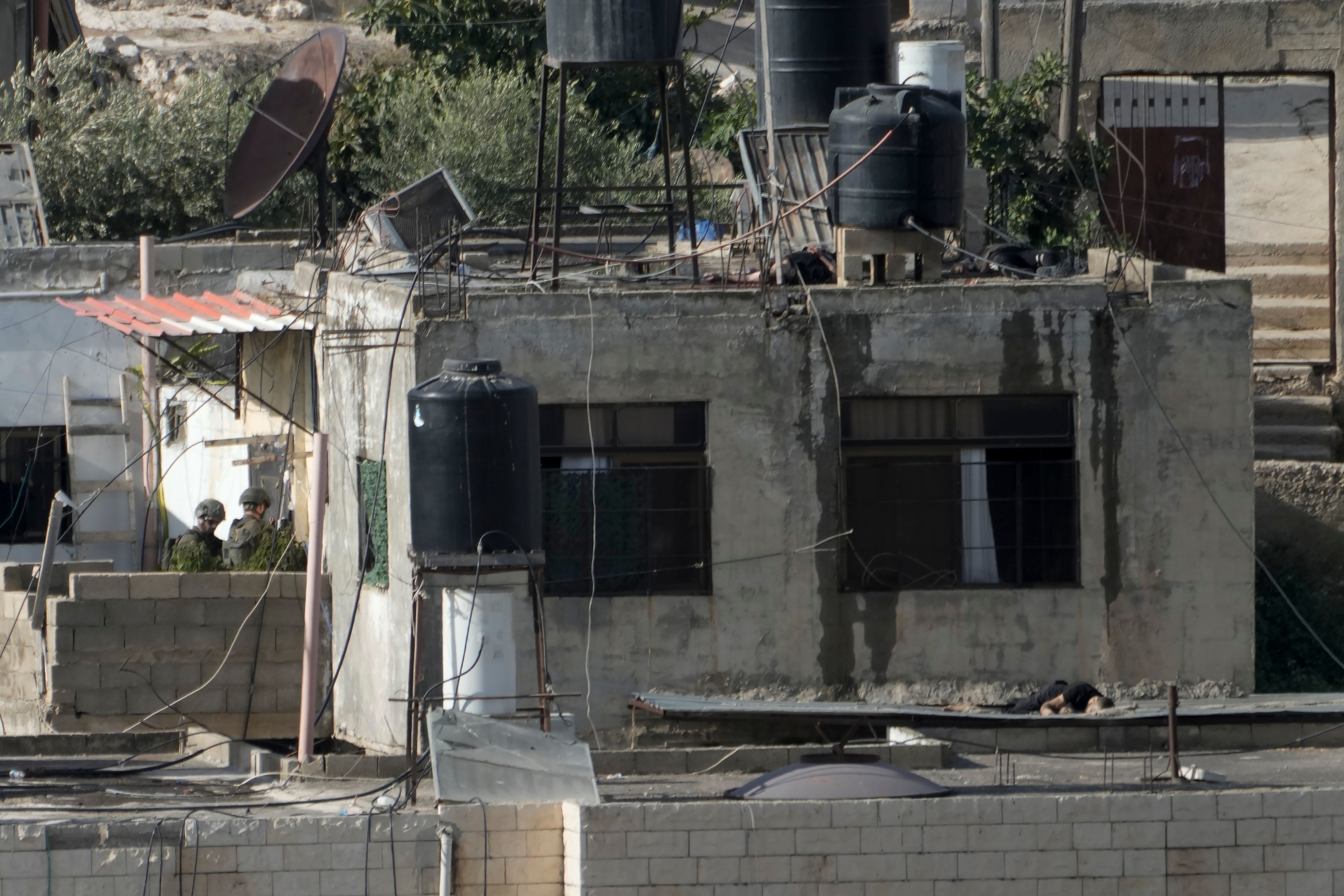 EDS NOTE: GRAPHIC CONTENT - Israeli soldiers stand near three bodies on rooftops in the West Bank town of Qabatiya during a raid, Thursday, Sept. 19, 2024. (AP Photo/Majdi Mohammed)