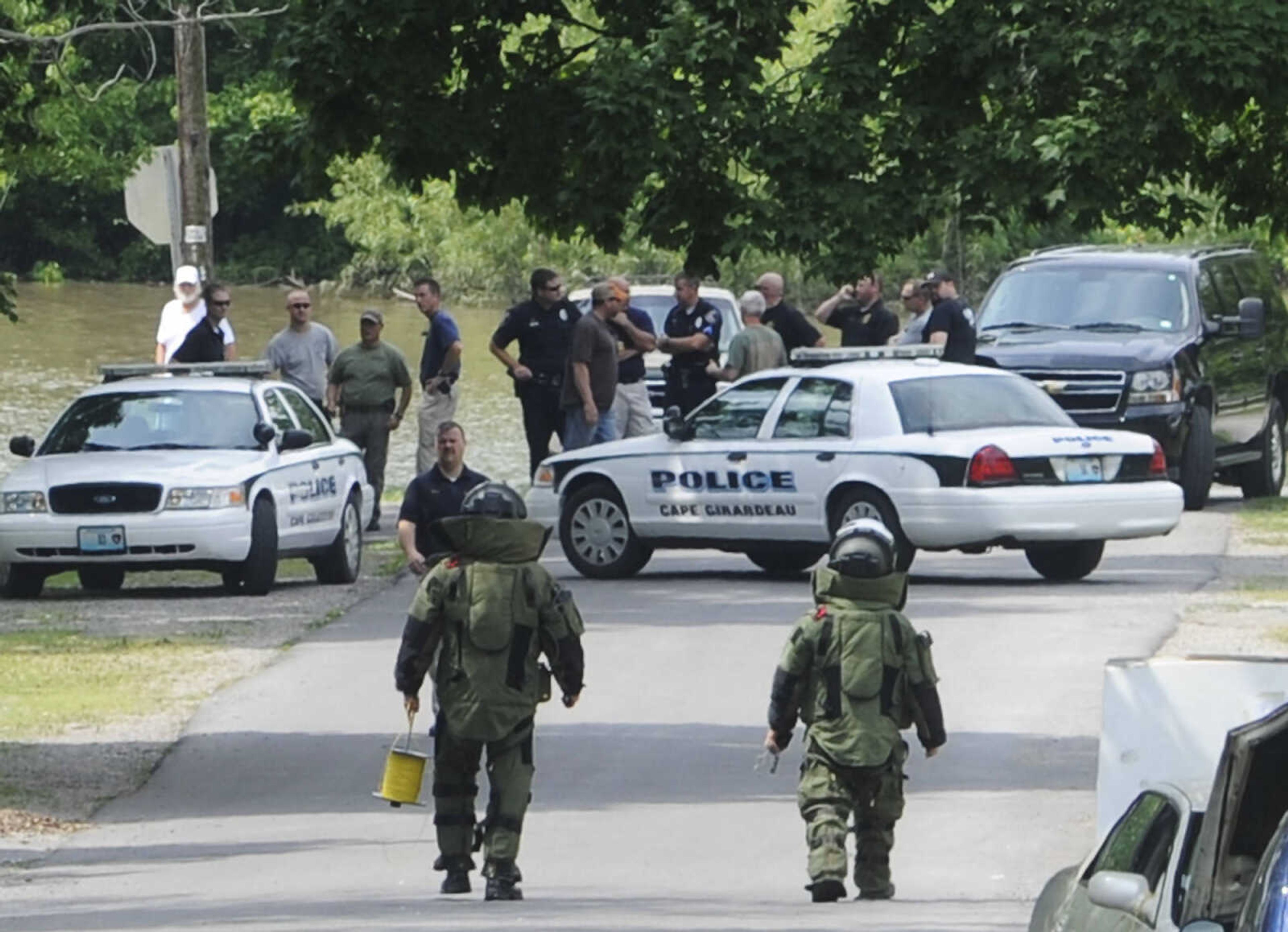 Two law enforcement officers in protective suits walk away from a Cadillac parked on the 1200 block of North Spanish Street Sunday, June 9. An unidentified man detonated an explosive in the vehicle Sunday morning while parked in front of the residence of his estranged wife injuring himself. (Adam Vogler)