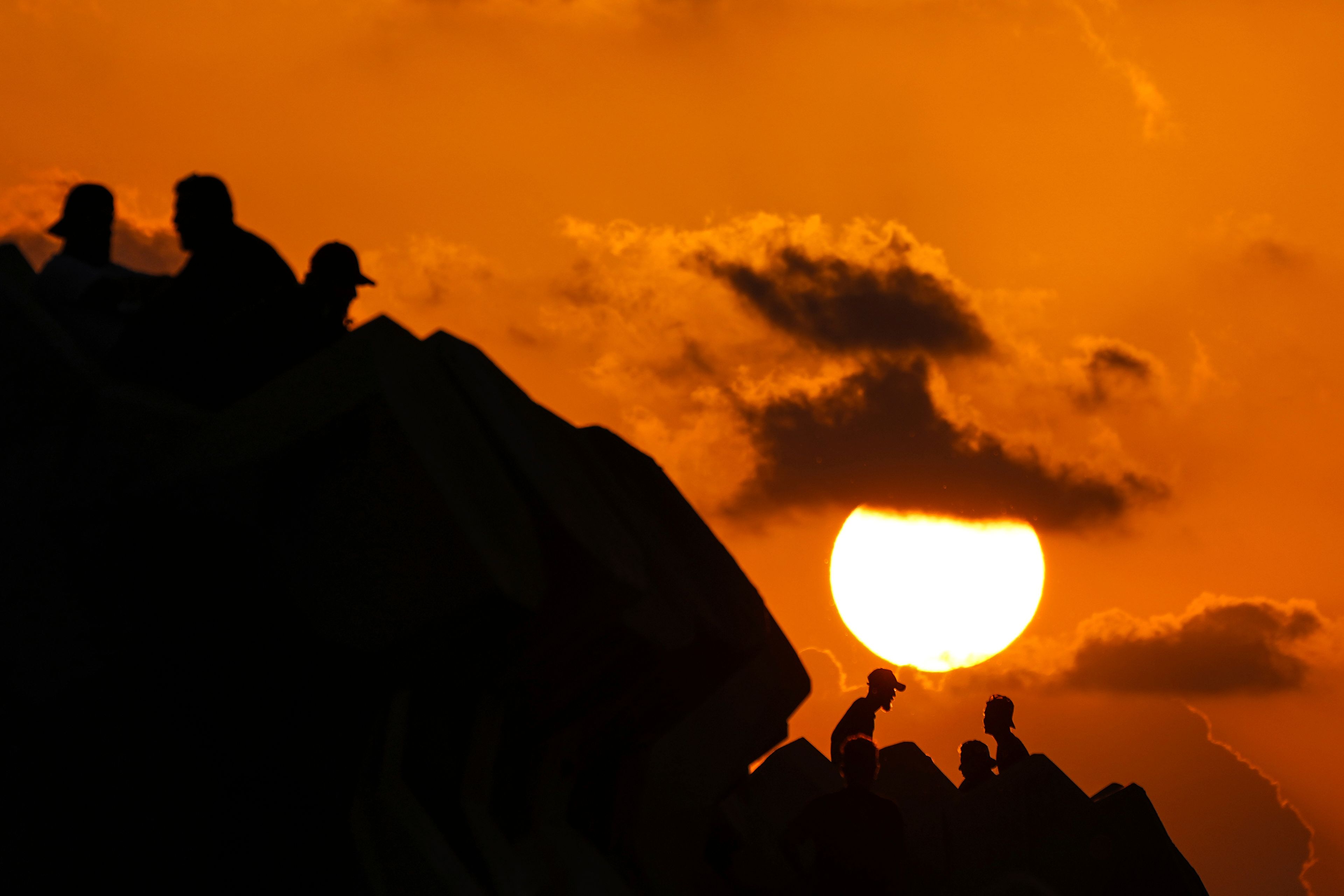 Displaced men fleeing the Israeli airstrikes in Beirut's Dahiyeh suburb, sit at Beirut's seaside promenade, along the Mediterranean Sea while the sun sets over the capital Beirut, Lebanon, Thursday, Oct. 17, 2024. (AP Photo/Hassan Ammar)