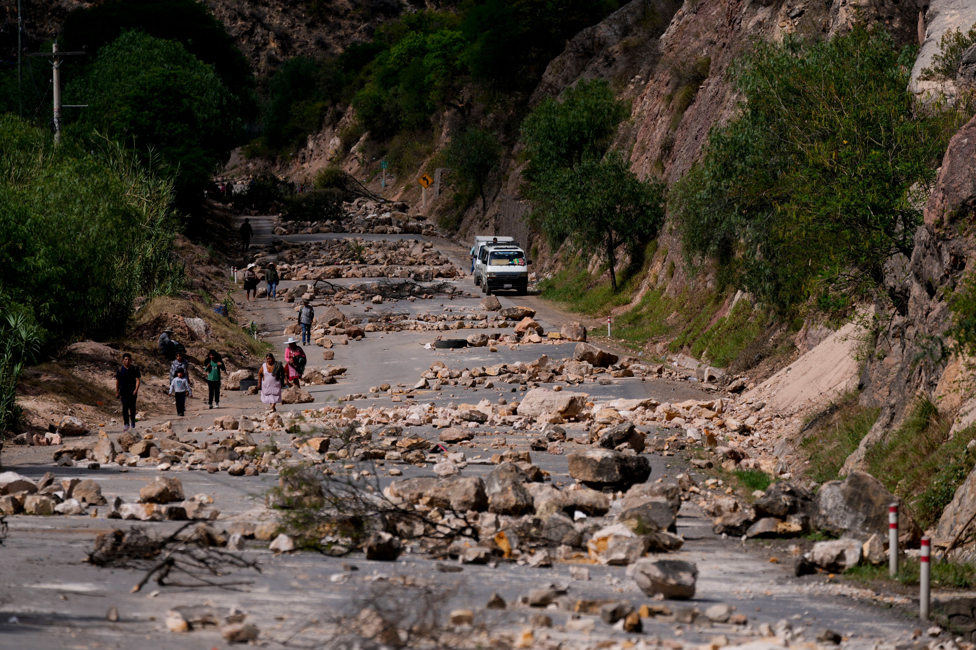 Pedestrians walk along a road blanketed with stones placed by supporters of Bolivian former President Evo Morales to prevent him from facing a criminal investigation over allegations of abuse of a minor and to demonstrate against an alleged assassination attempt, in Parotani, Bolivia, Tuesday, Oct. 29, 2024. (AP Photo/Juan Karita)