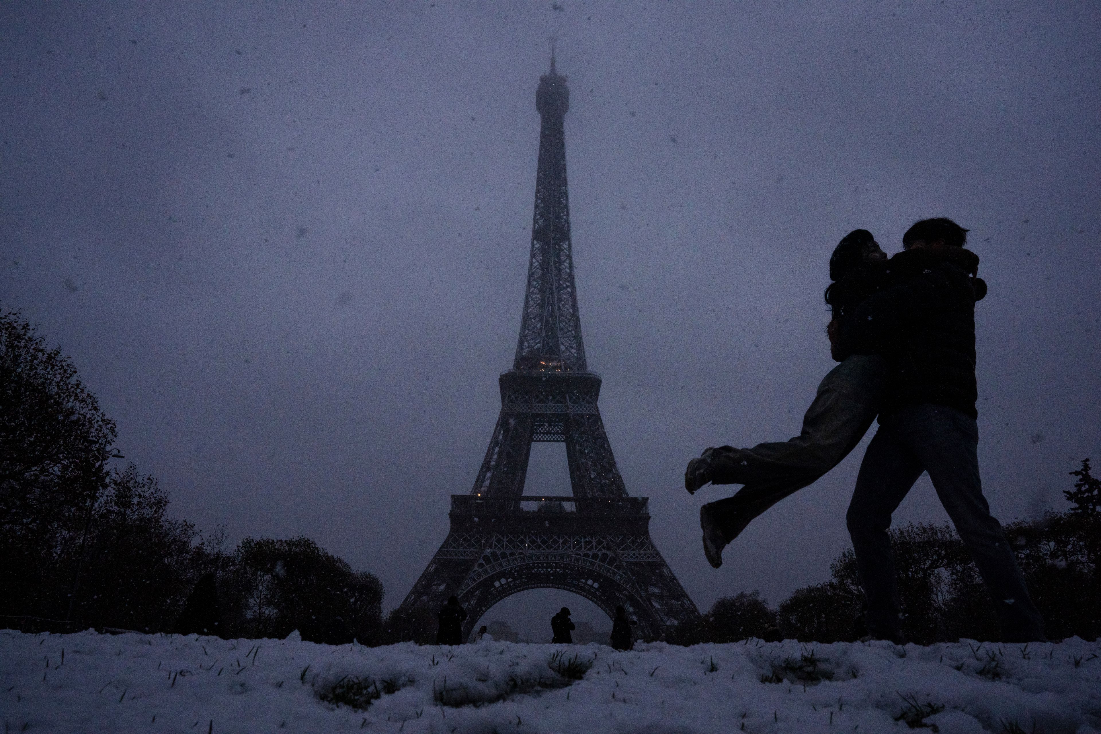 Visitors move as snow falls, with the Eiffel Tower in the background, in Paris, Thursday, Nov. 21, 2024. (AP Photo/Louise Delmotte)