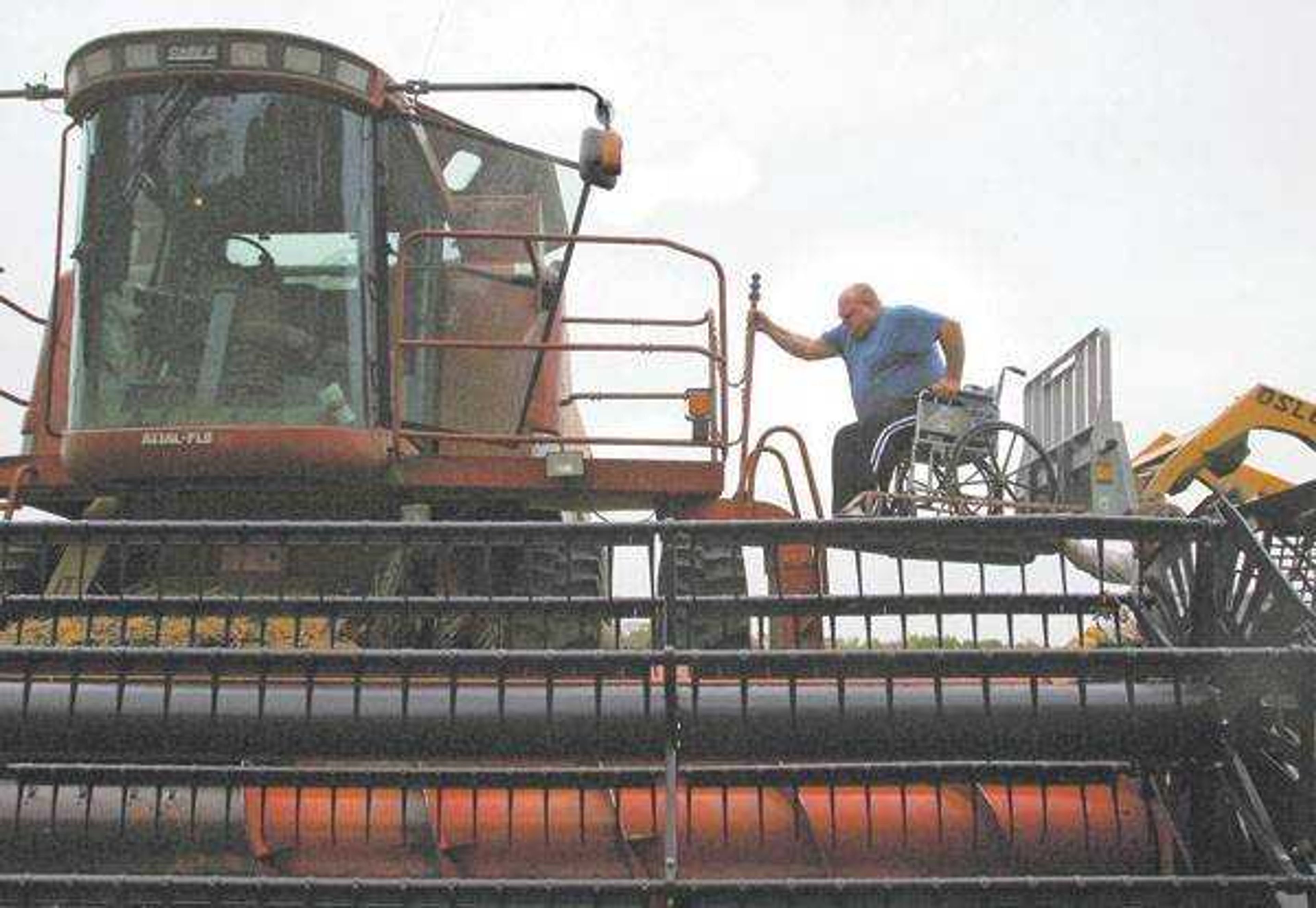 Andy Leake mounted a combine in his wheelchair with the aid of farm worker Tony Fischer, who was operating a skid loader with a homemade deck plate for Leake's wheelchair, on his farm near New London, Mo. Leake injured his back picking up a bag of seed after surgery and has limited use of his legs, yet he farms 3,000 acres. (Kevin Manning ~  St. Louis Post-Dispatch)