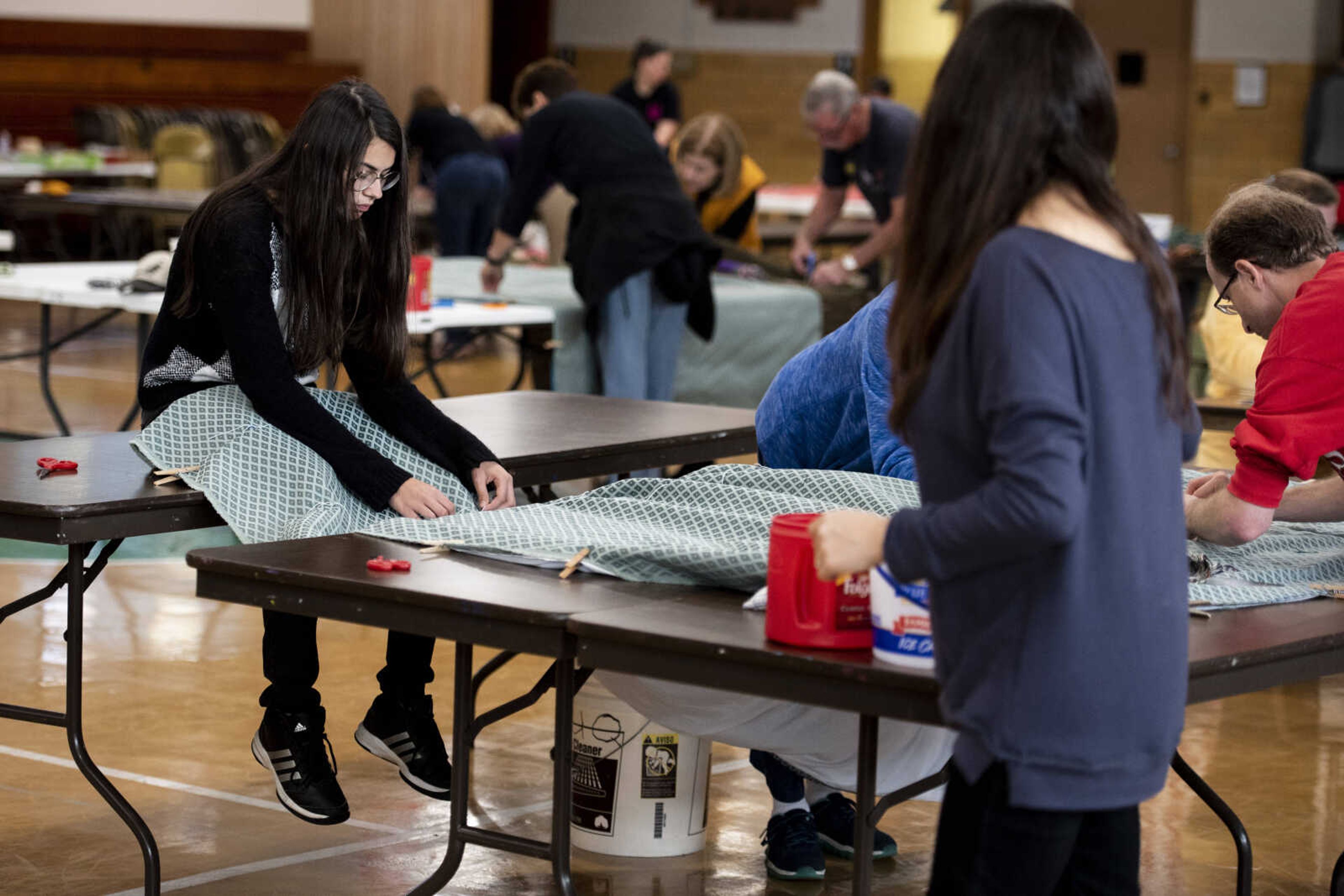 Sophia Robison, left, sits on top of a table while tacking a bed roll quilt during the Ugly Quilt Weekend at St. Vincent de Paul Parish Sunday, Oct. 28, 2018, in Cape Girardeau.