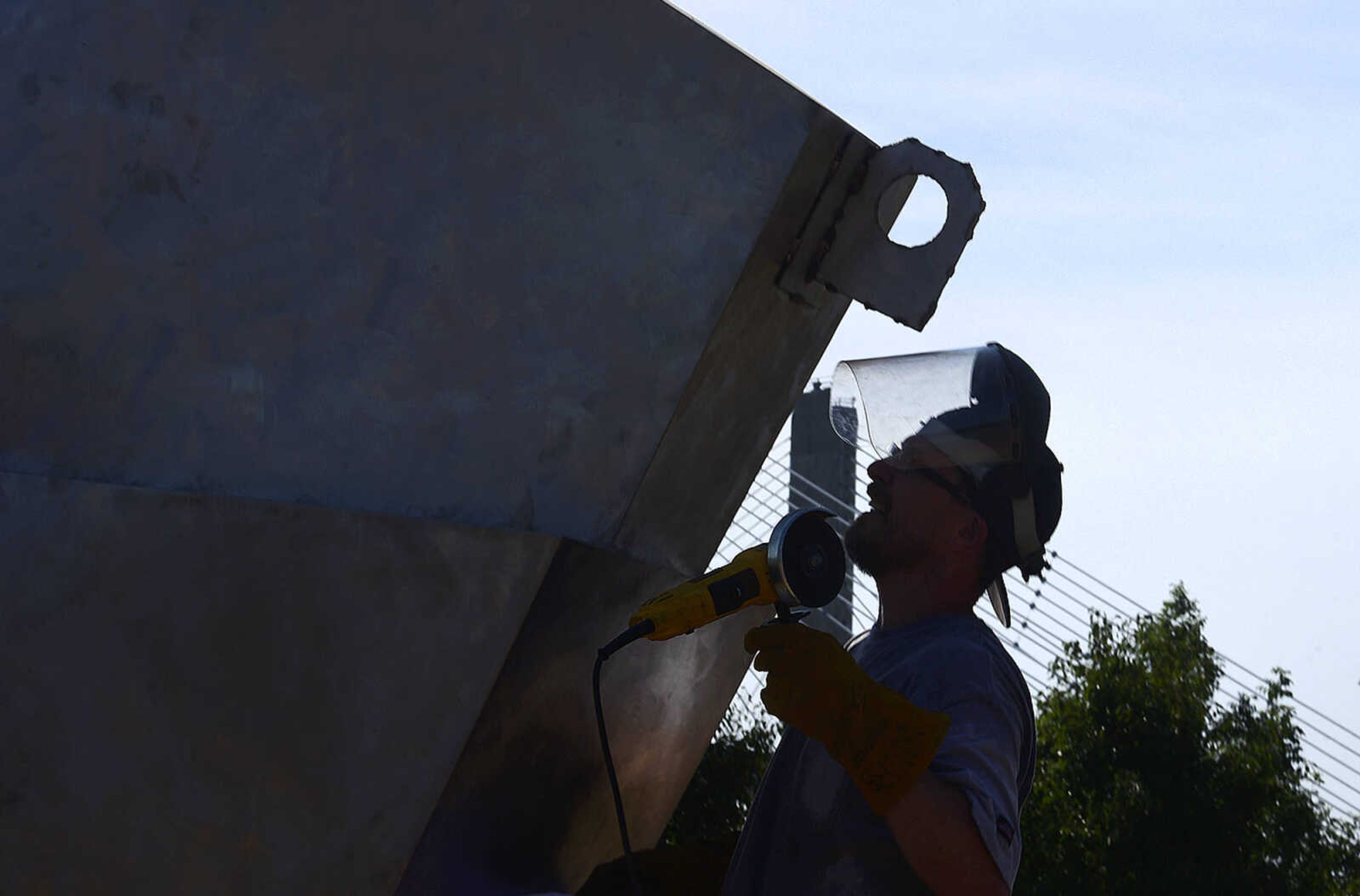 Chris Wubbena cuts an eyelet off of his sculpture, "Commence" that was used to help install the two-piece 14-foot sculpture in the Fountain Street roundabout on Monday, July 24, 2017, near the River Campus in Cape Girardeau.