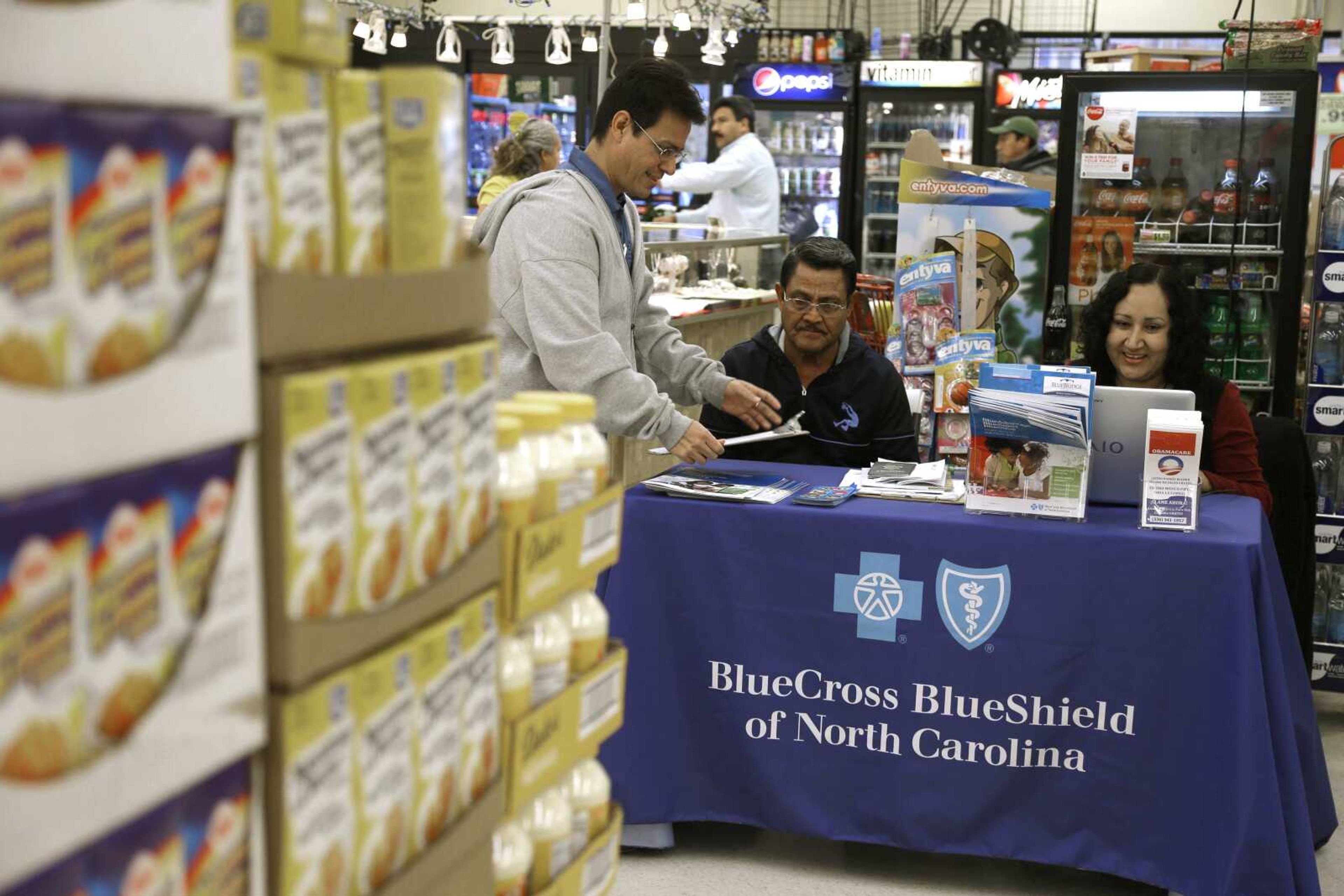 Blue Bridge Benefits LLC agent Patricia Sarabia, right, and Adolfo Briceno, left, of Spanish Speaking LLC, help a potential customer with Blue Cross Blue Shield at a kiosk promoting health insurance under the federal Affordable Care Act at Compare Foods in Winston-Salem, North Carolina.