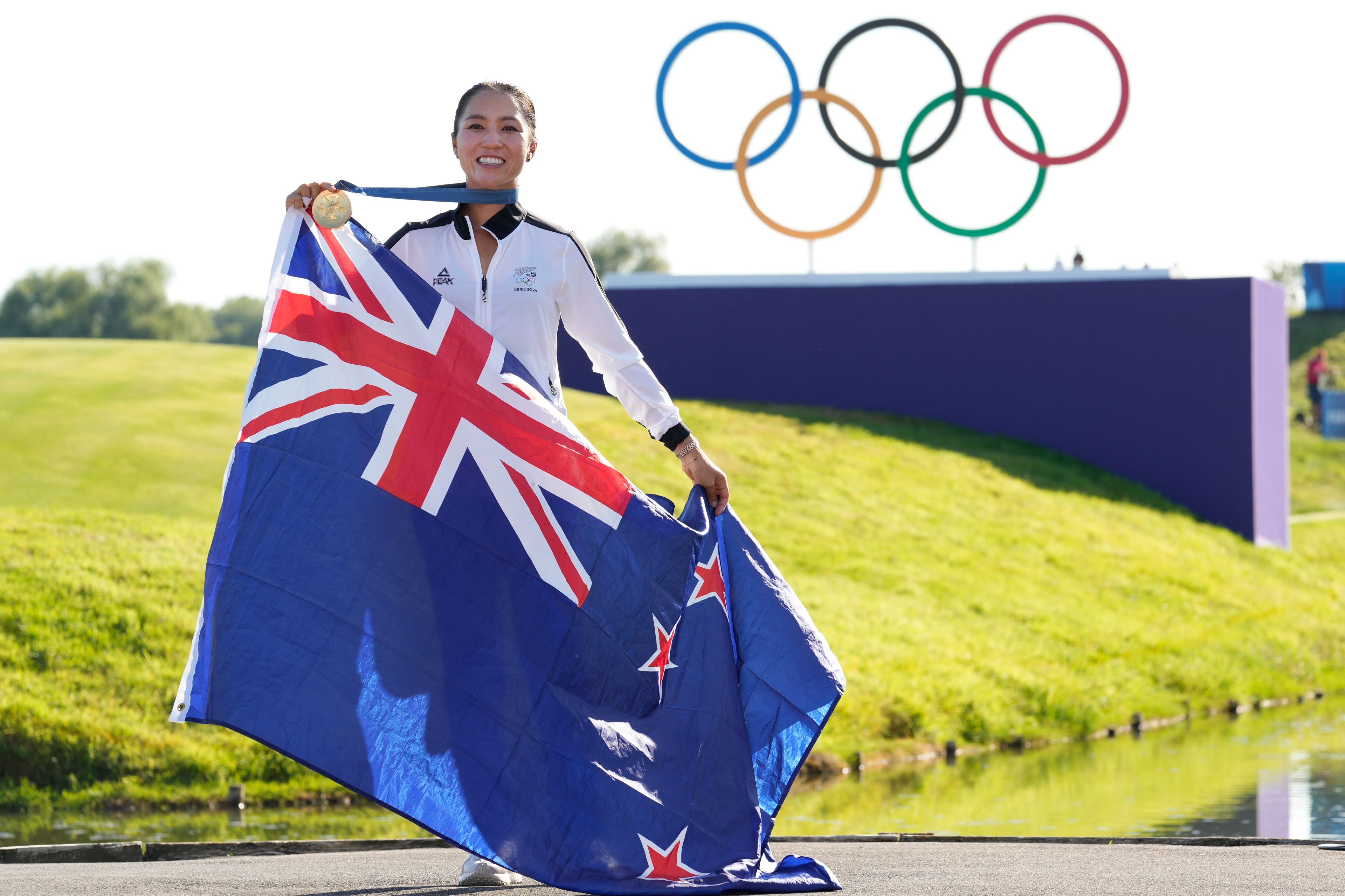 Lydia Ko, of New Zealand, poses for the cameras with her gold medal, and the New Zealand flag following final round of the women's golf event at the 2024 Summer Olympics, Saturday, Aug. 10, 2024, at Le Golf National, in Saint-Quentin-en-Yvelines, France. (AP Photo/Matt York)