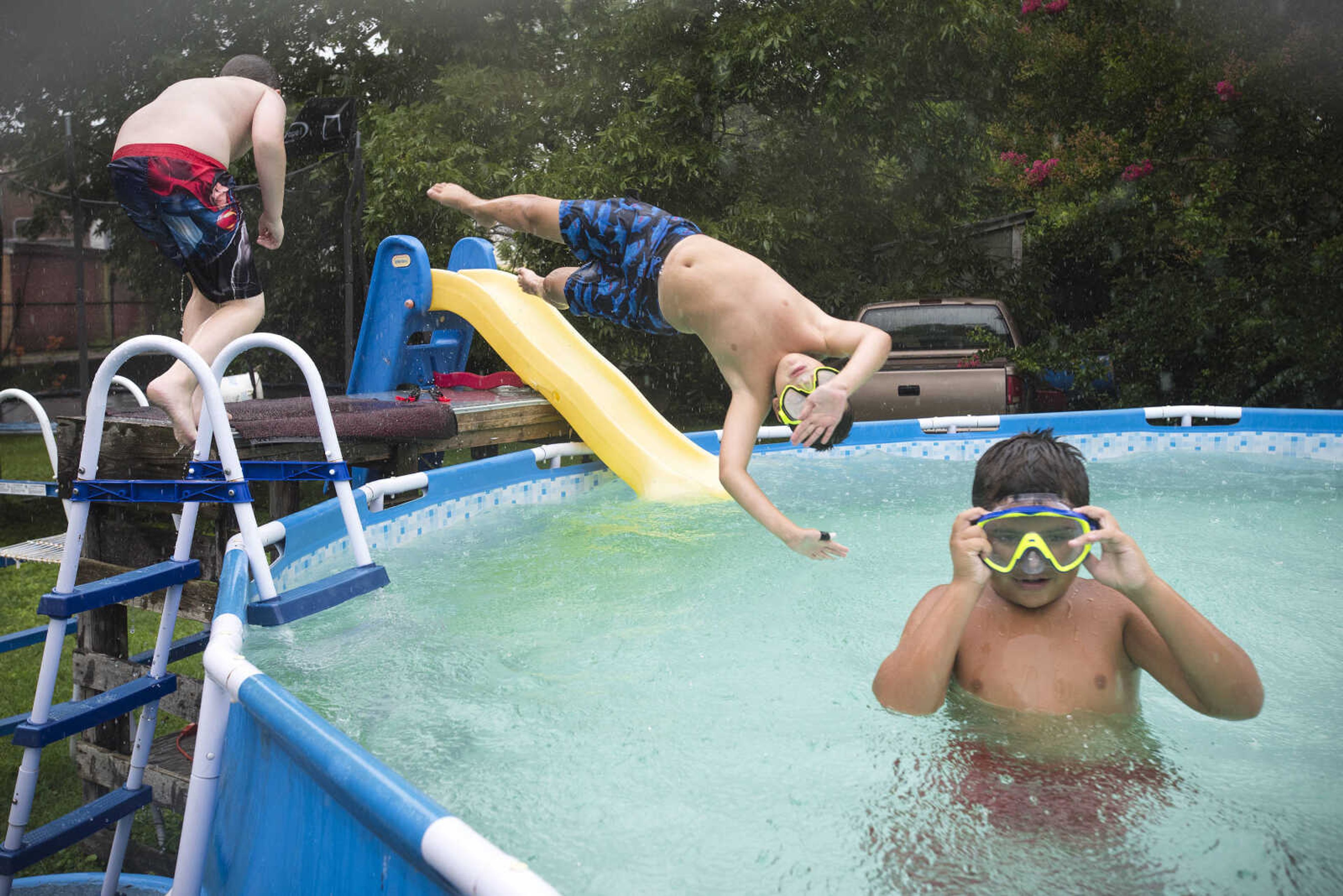 After spending the morning at vacation Bible school, Nicholas Elfrink, center, leaps into the pool while swimming with John Paul Barinque, right, and Declan Vowels, left, as an afternoon rain shower begins to fall Tuesday, July 16, 2019, in Cape Girardeau.