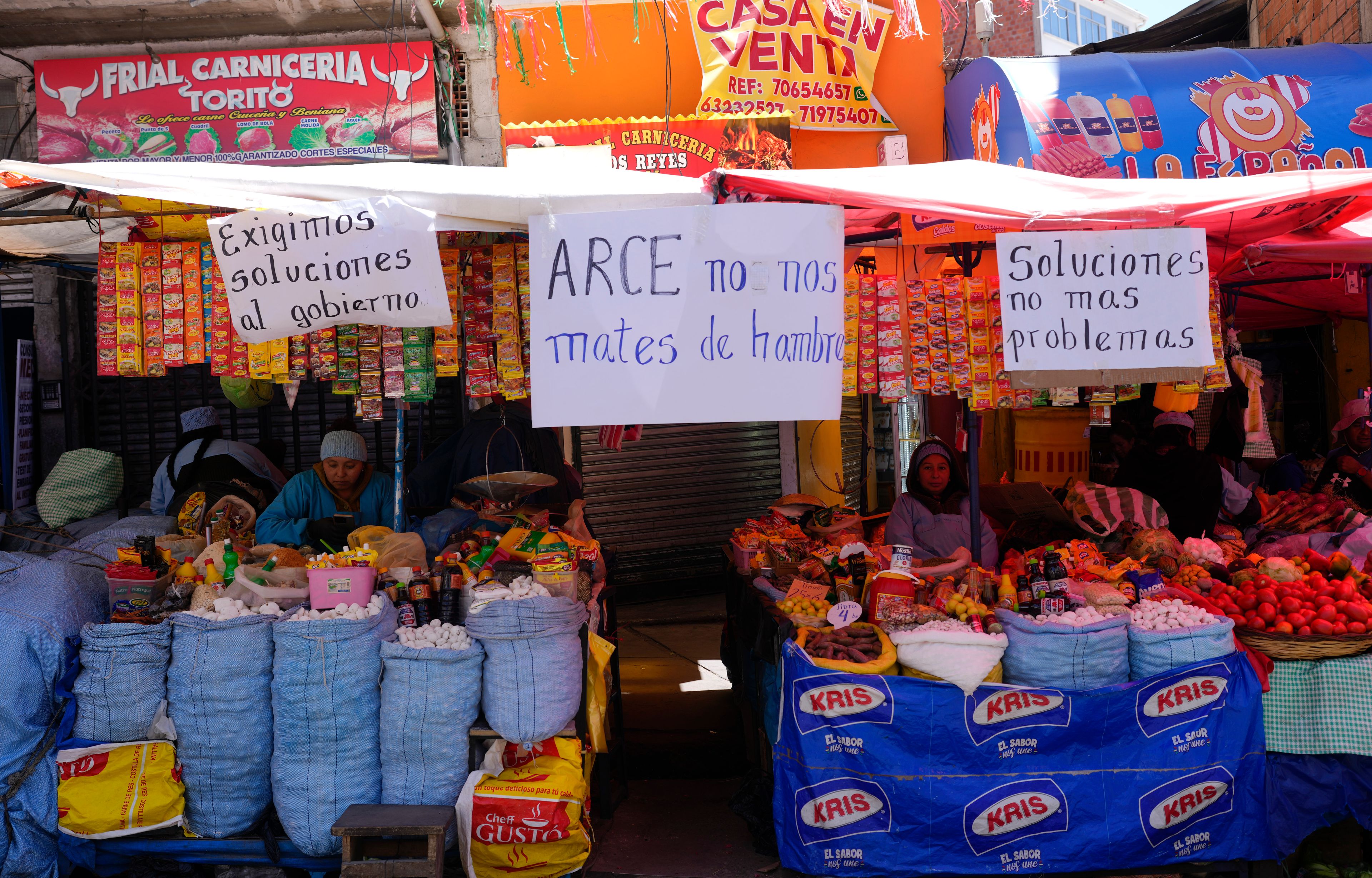 FILE - Handwritten sign with messages that read in Spanish: "We demand solutions from the government", "Arce, don't starve us" and "Solutions, not more problems", hang from vendors' stalls at a street market in La Paz, Bolivia, Oct. 21, 2024. (AP Photo/Juan Karita, File)