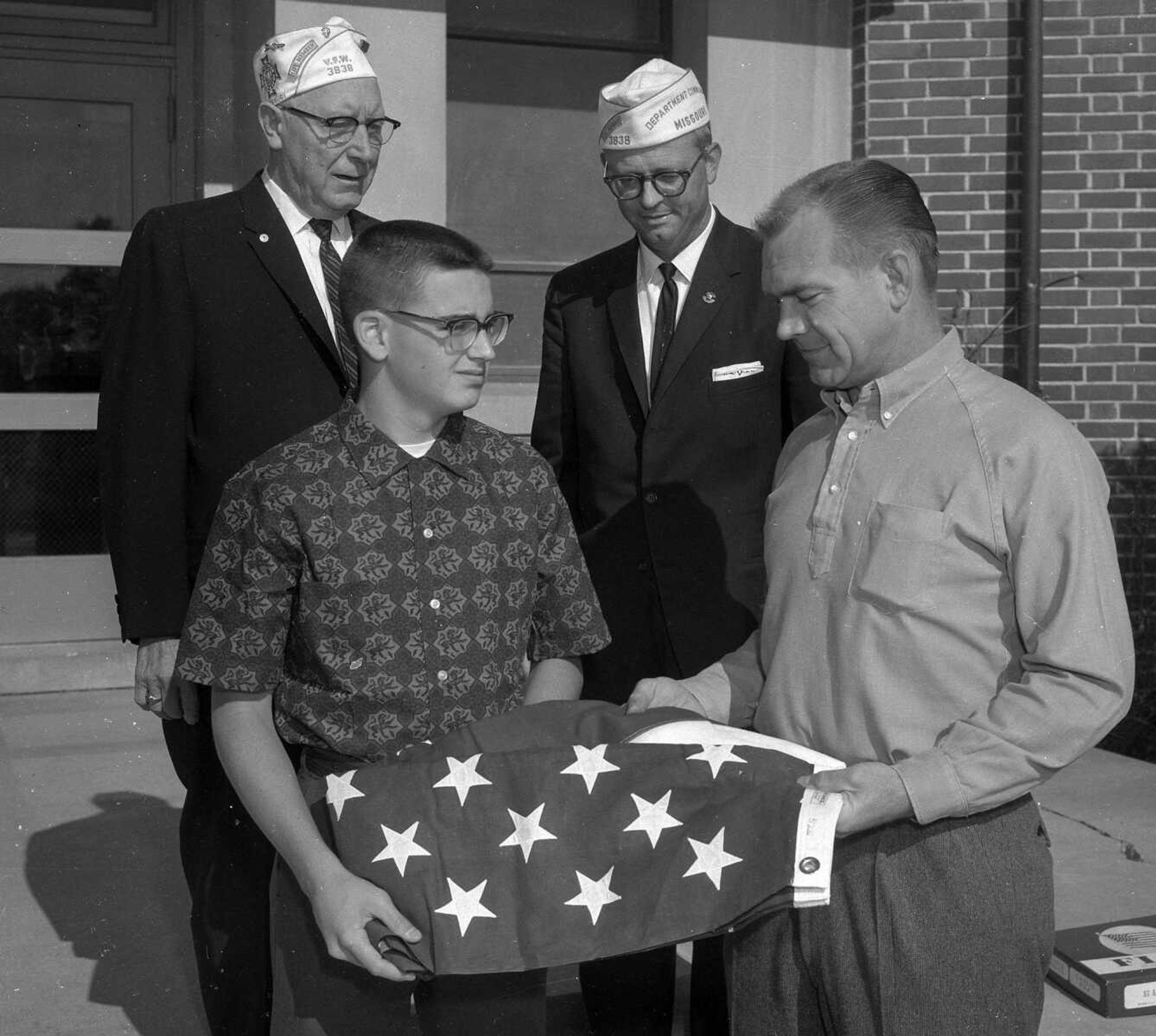 James Reynolds, Central High School junior, received a flag from Jerry Wilkening, Americanism chairman for the VFW post here for submitting the best Americanism slogan. Looking on were John Penn, left, post commander, and Calvin Vogelsang, state commander. (Missourian archive photo by G.D. Fronabarger)