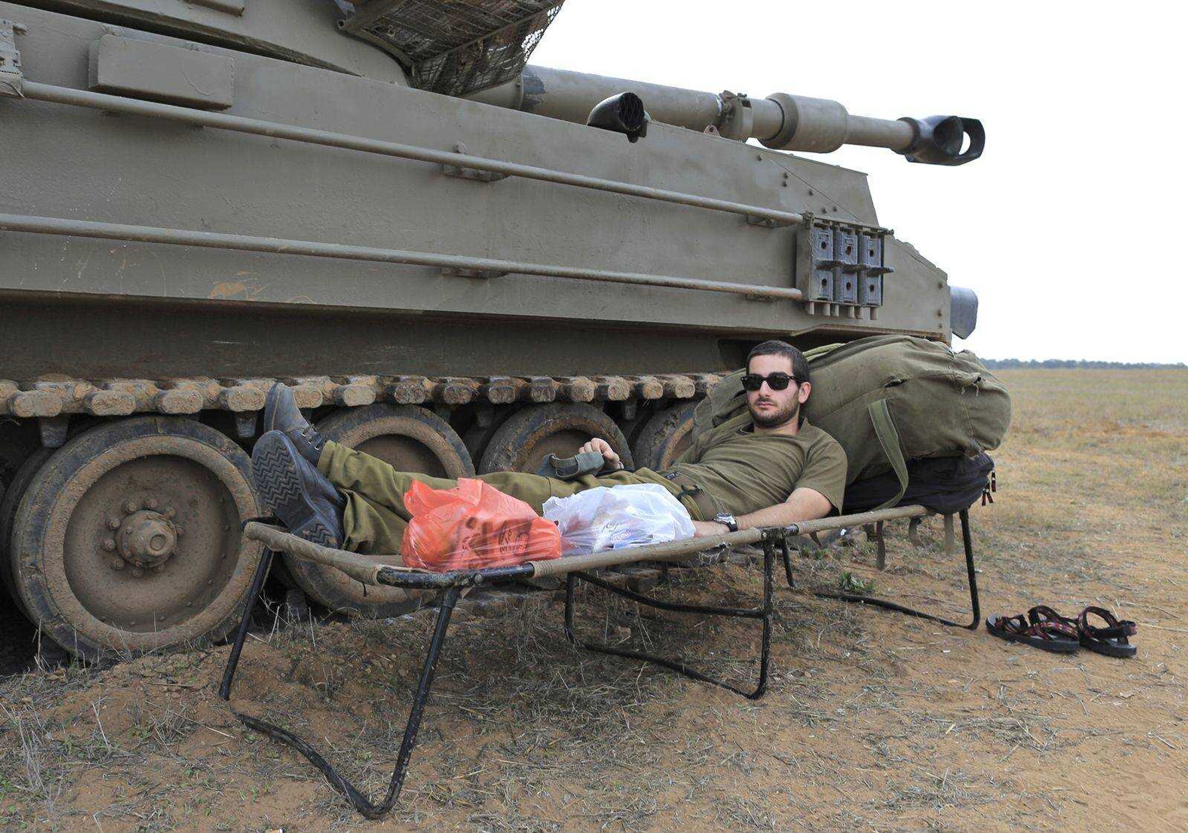 An Israeli soldier rests next to a mobile artillery vehicle Thursday at a staging area near the Israel Gaza Strip Border, southern Israel. (Tsafrir Abayov ~ Associated Press)