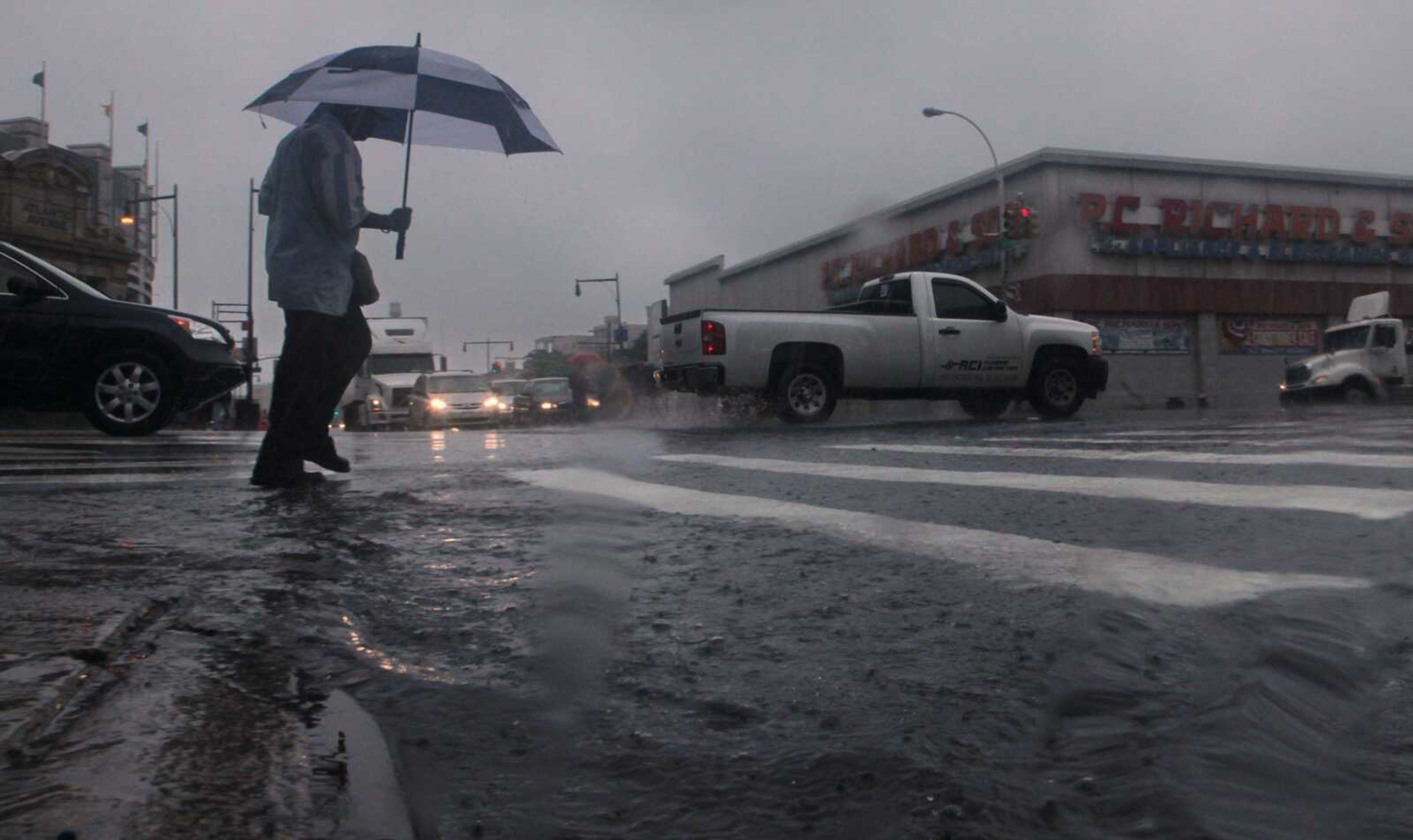 A pedestrian takes shelter under an umbrella while walking around a puddle during heavy rainfall Thursday in Brooklyn, N.Y. (Bebeto Matthews ~ Associated Press)