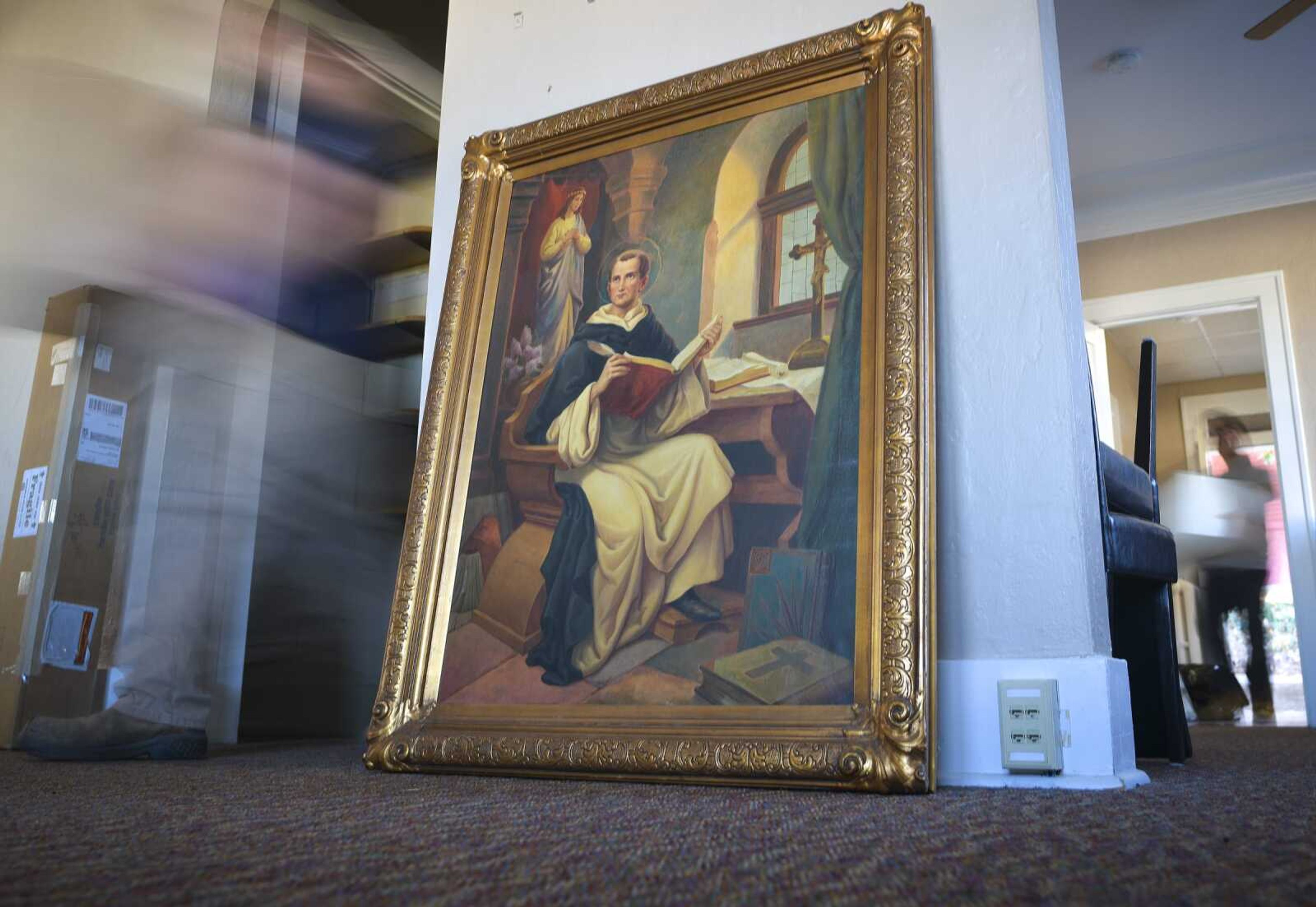 The Newman Center's portrait of St. Thomas Aquinas rests on the ground Thursday inside the Catholic Campus Ministry's interim location at 902 College Hill Place in Cape Girardeau as moving crews from Adult and Teen Challenge Mid-America unload boxes of office materials.