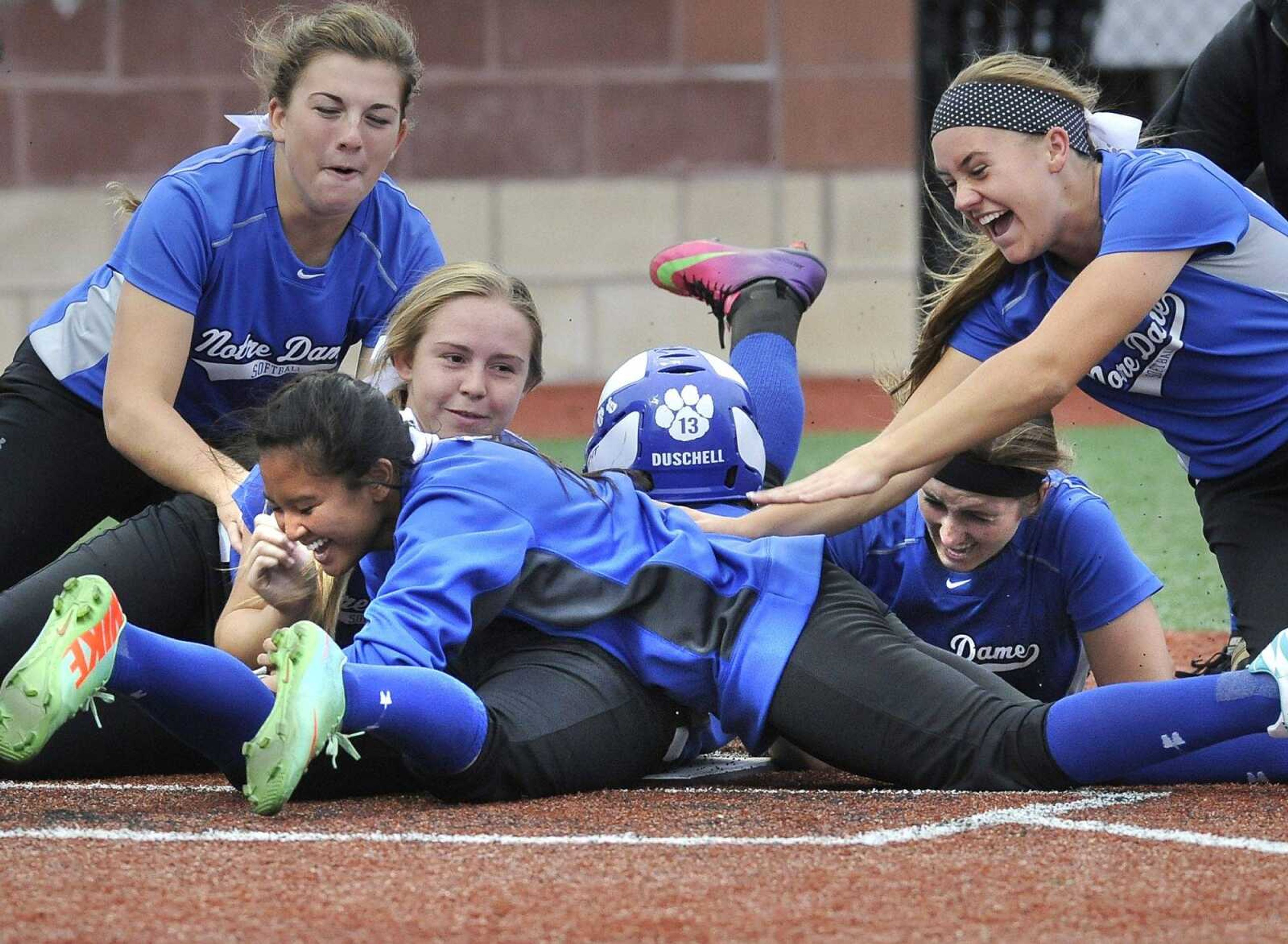 Notre Dame players celebrate their 11-1 victory over Sikeston by piling on Morgan Duschell after she scored their final run to end the Class 3 District 1 title game.