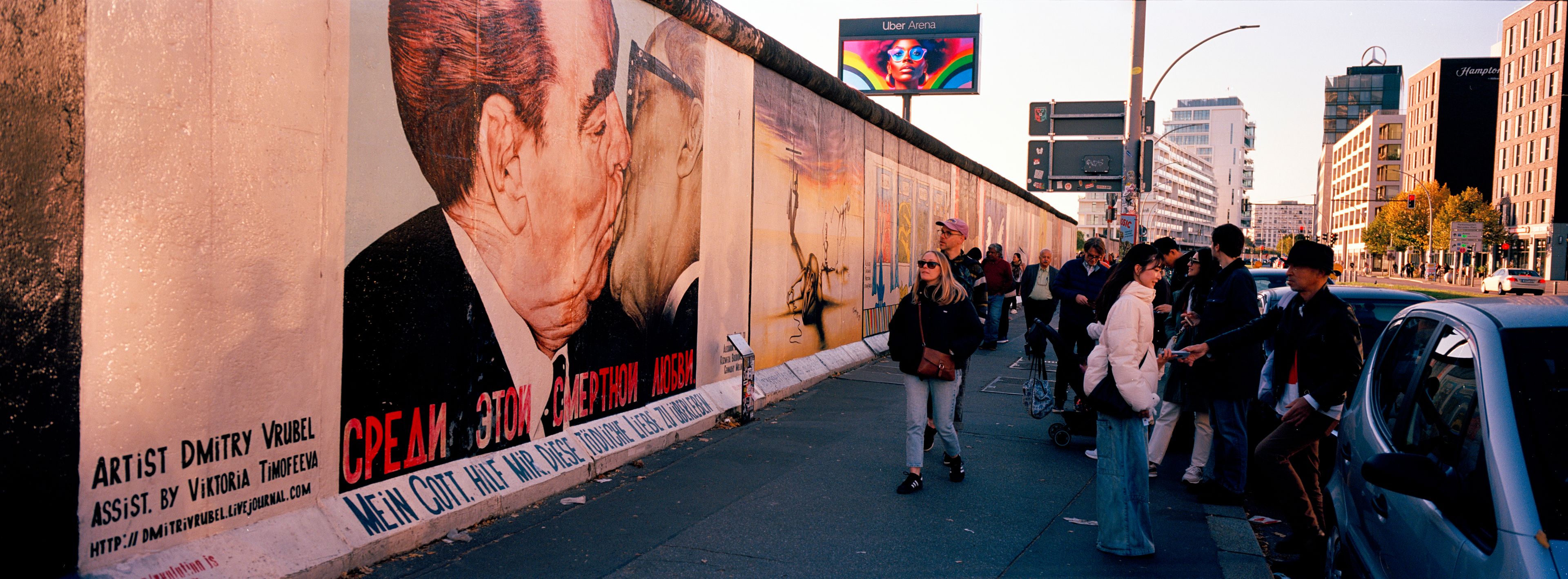 People gather at a paining of former Soviet leader Leonid Brezhnev, left, kissing former East German leader Erich Honecker at the so called East Side Gallery, a popular place for street art on remains of Berlin Wall in Berlin, Germany, Tuesday, Oct. 15, 2024. (AP Photo/Markus Schreiber)