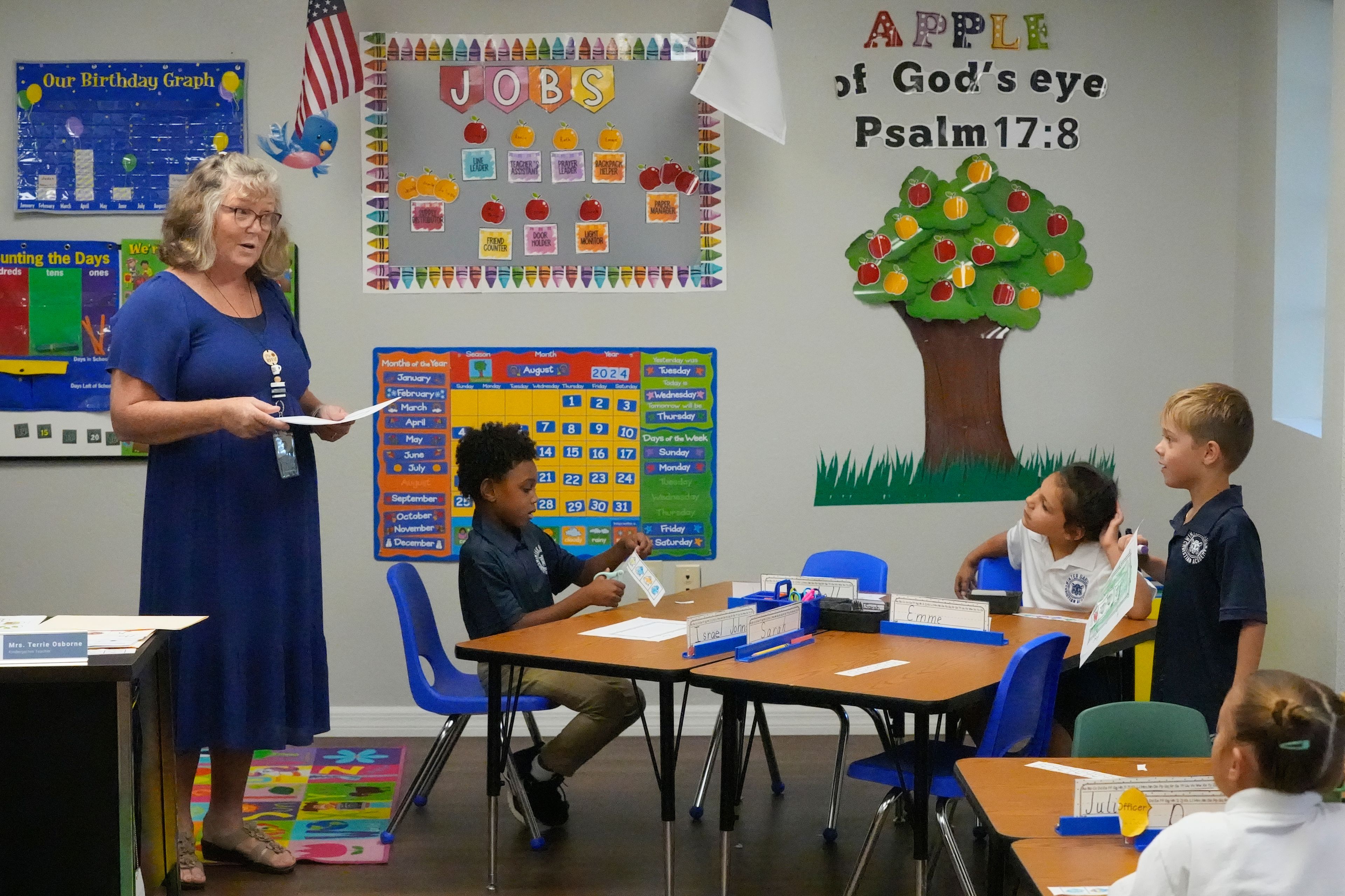 Kindergarten teacher Terrie Osborne helps students in her class at the Winter Garden Christian Academy Thursday, Aug. 29, 2024, in Winter Garden, Fla. (AP Photo/John Raoux)