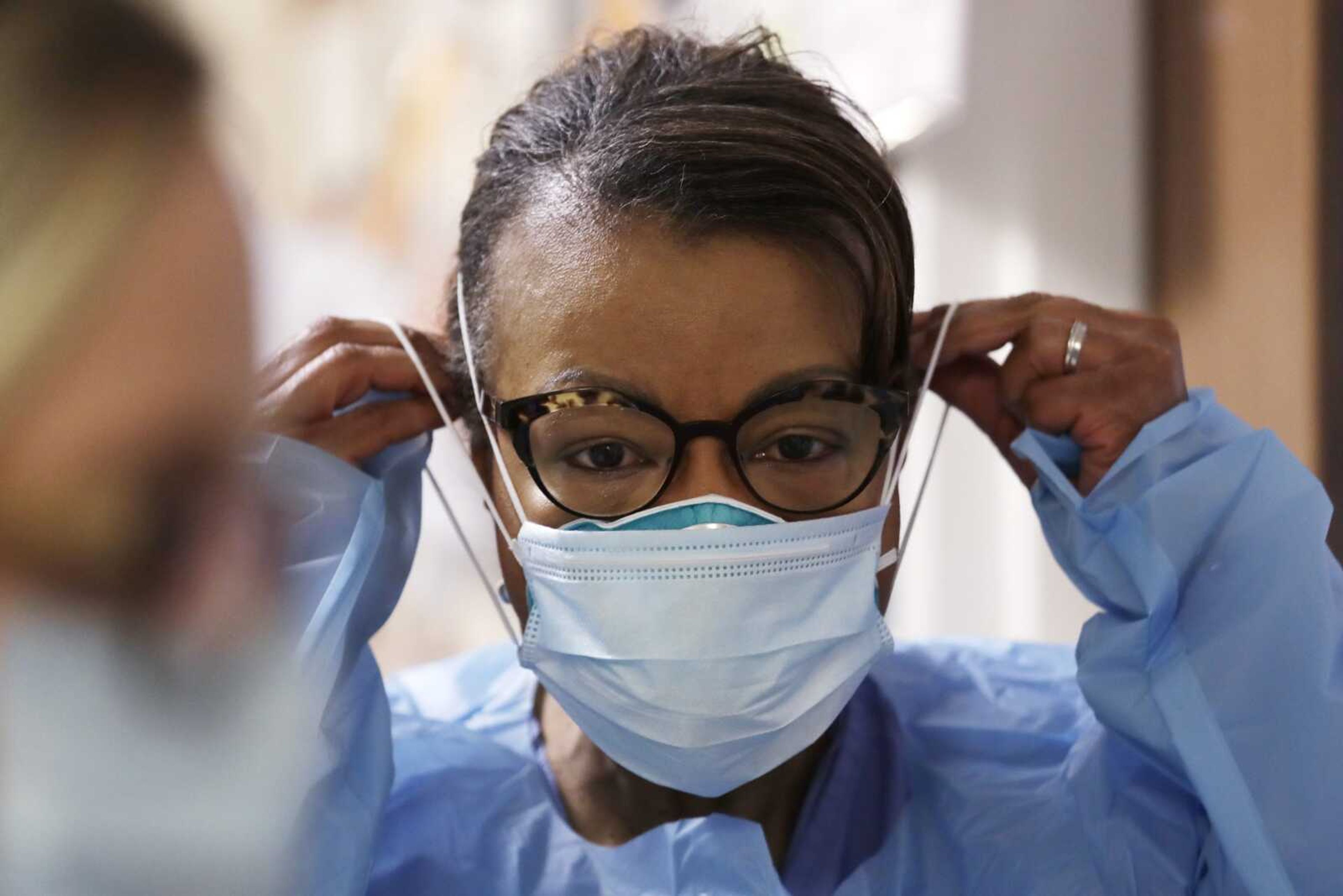 A respiratory therapist pulls on a second mask over her N95 mask before adding a face shield as she gets ready to go into a patient's room in the COVID-19 Intensive Care Unit at a hospital in Seattle.  Medical providers may soon return to using one medical N95 mask per patient, a practice that was suspended during the pandemic due to deadly supply shortages.