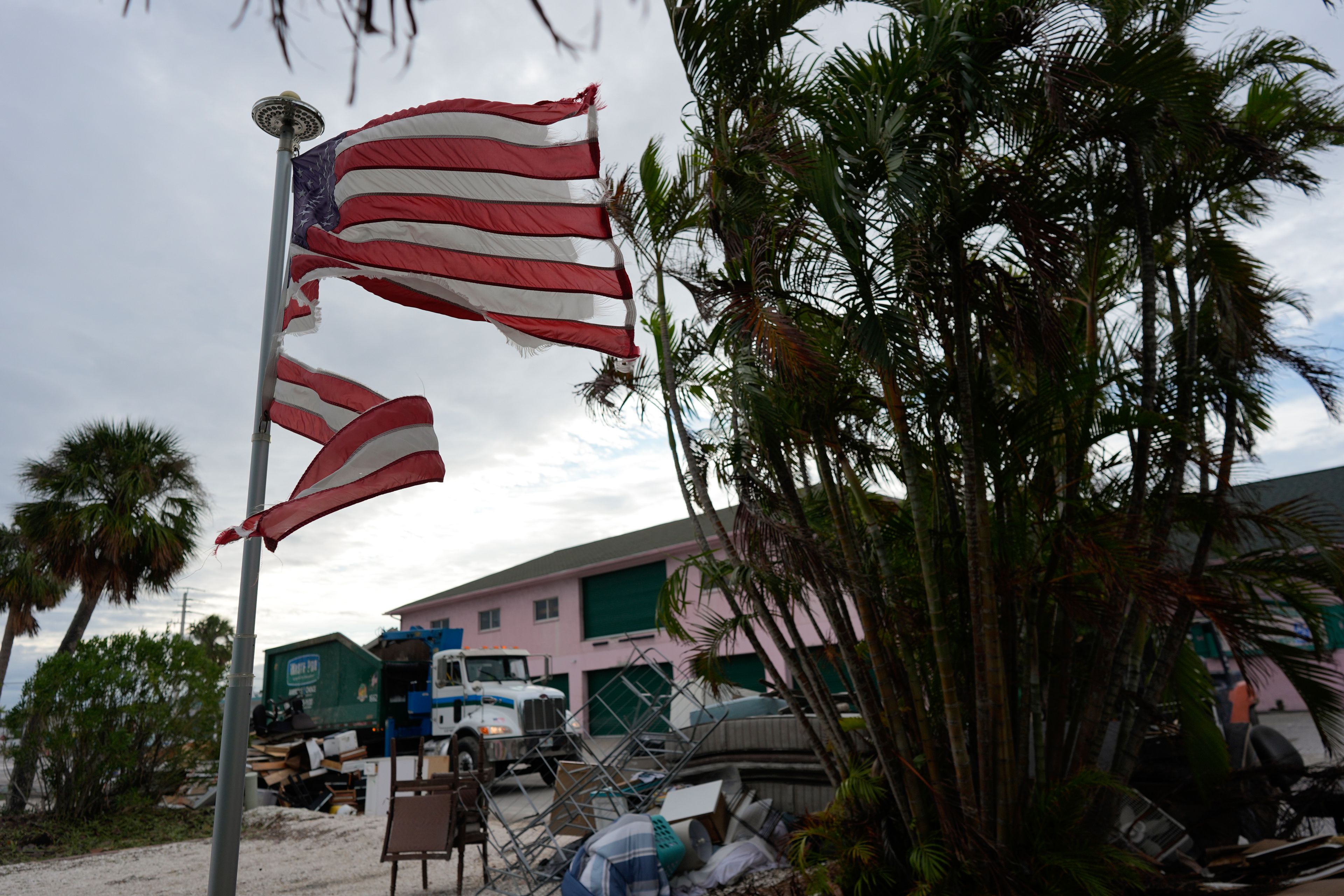 A tattered American flag flaps outside a home as crews work to clean up piles of debris from Hurricane Helene flooding ahead of the arrival of Hurricane Milton, in Holmes Beach on Anna Maria Island, Fla., Tuesday, Oct. 8, 2024. (AP Photo/Rebecca Blackwell)