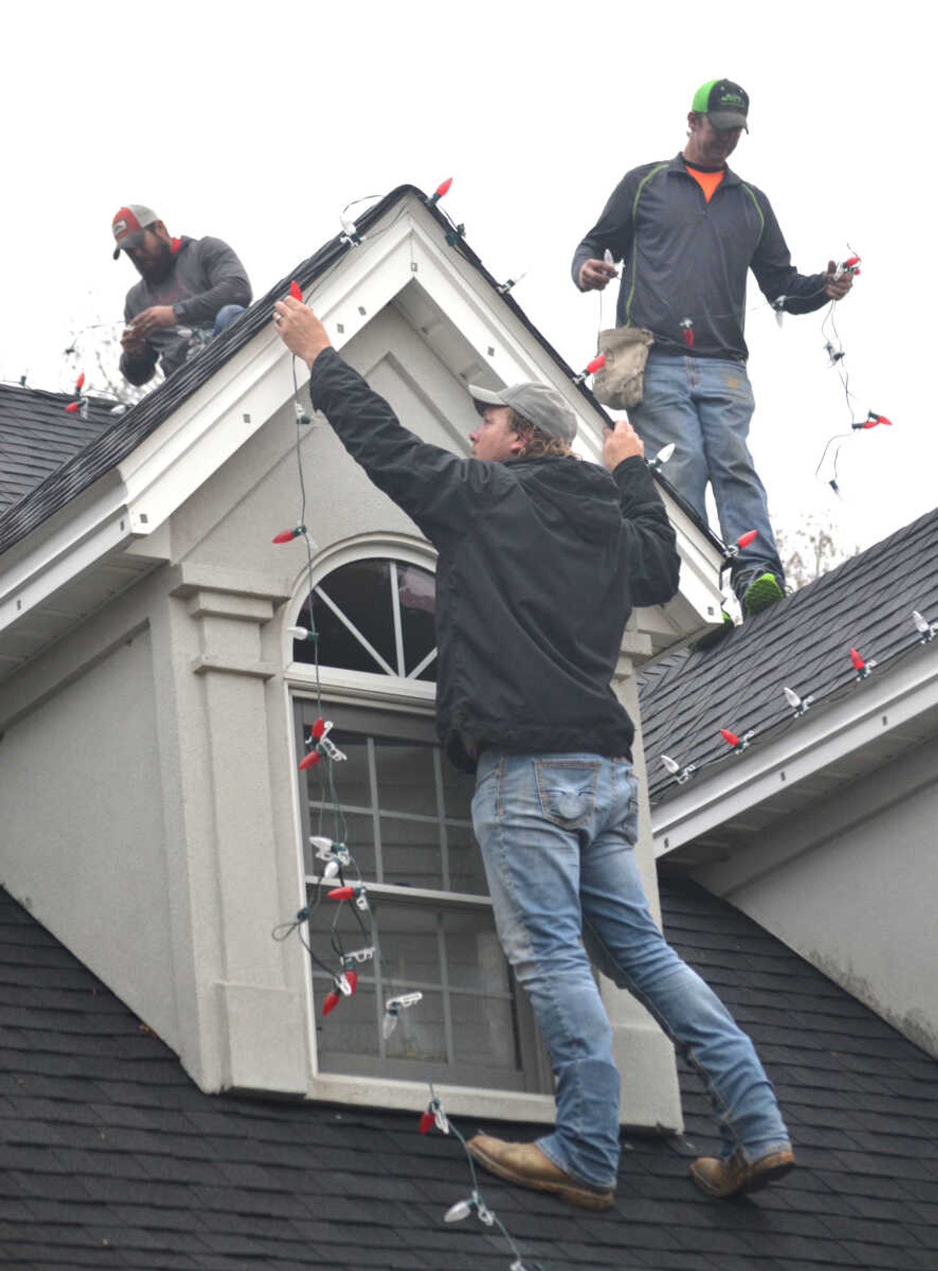 Chris Vernon, left, C.B. Forck, foreground, and Brent Forck hang lights last week along the roofline at the home of Vince and Jan Kelley in Cape Girardeau.