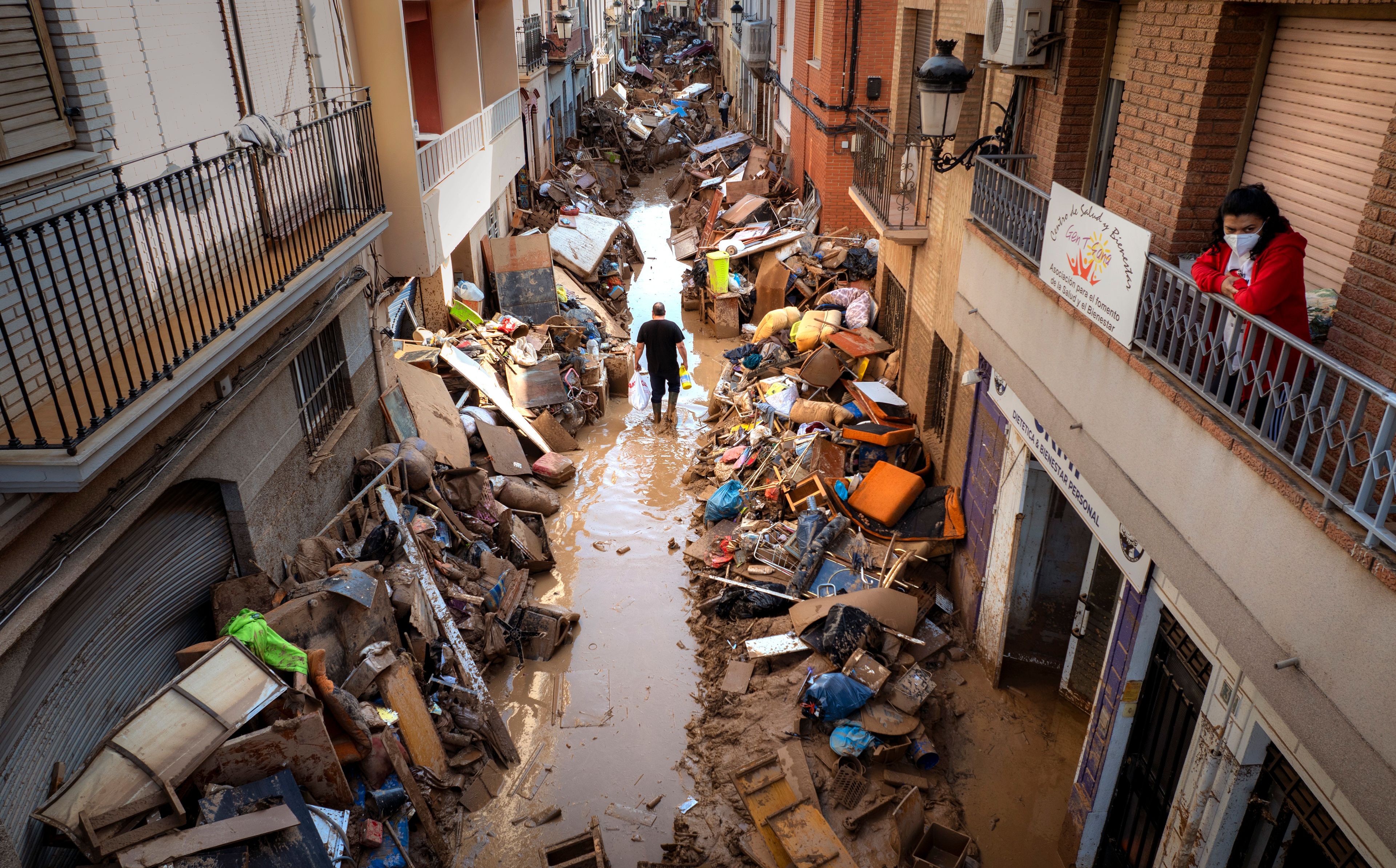 People walk through a street with piled furniture and rubbish on the sides in an area, affected by floods, in Paiporta, Valencia, Spain, Tuesday, Nov. 5, 2024. (AP Photo/Emilio Morenatti)