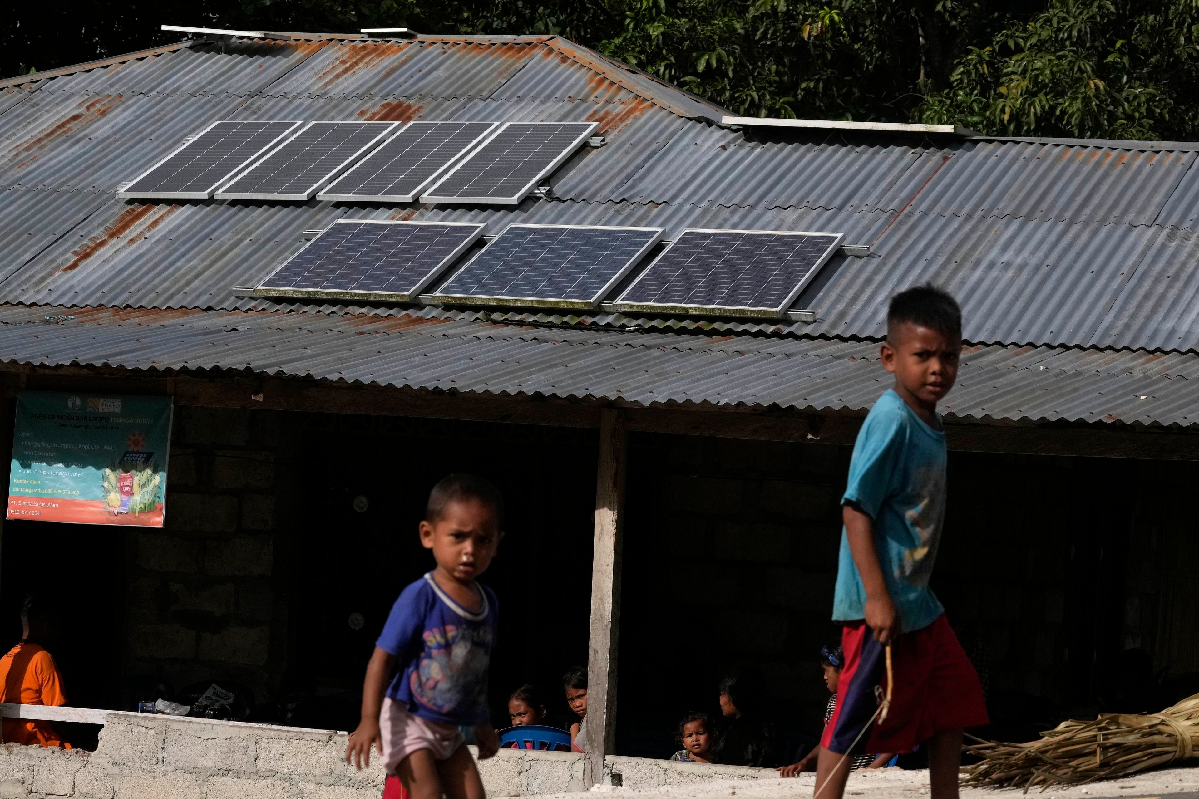 FILE - Children play near solar panels on the roof of house in Walatungga village on Sumba Island, Indonesia, March 21, 2023. (AP Photo/Dita Alangkara)