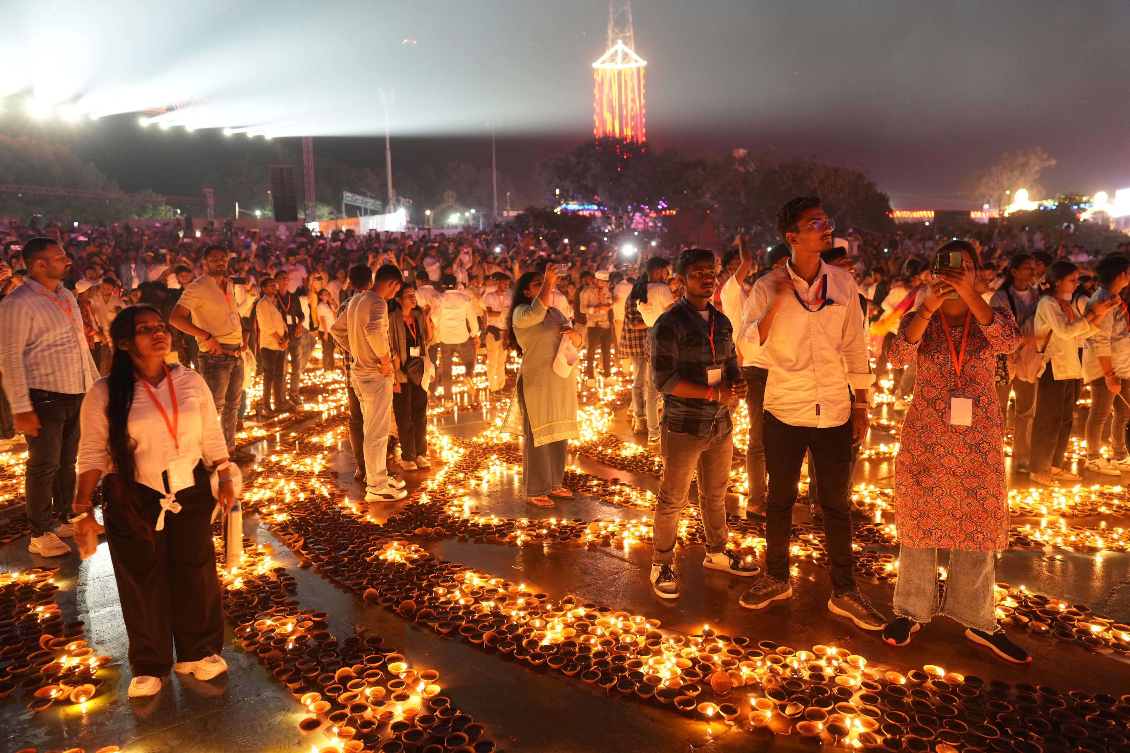 People stand in between rows of lit earthen lamps on the banks of the Saryu river during Deepotsav celebrations, an event organized by the Uttar Pradesh state government on the eve of Diwali, in Ayodhya, India, Wednesday, Oct. 30, 2024. (AP Photo/Rajesh Kumar Singh)