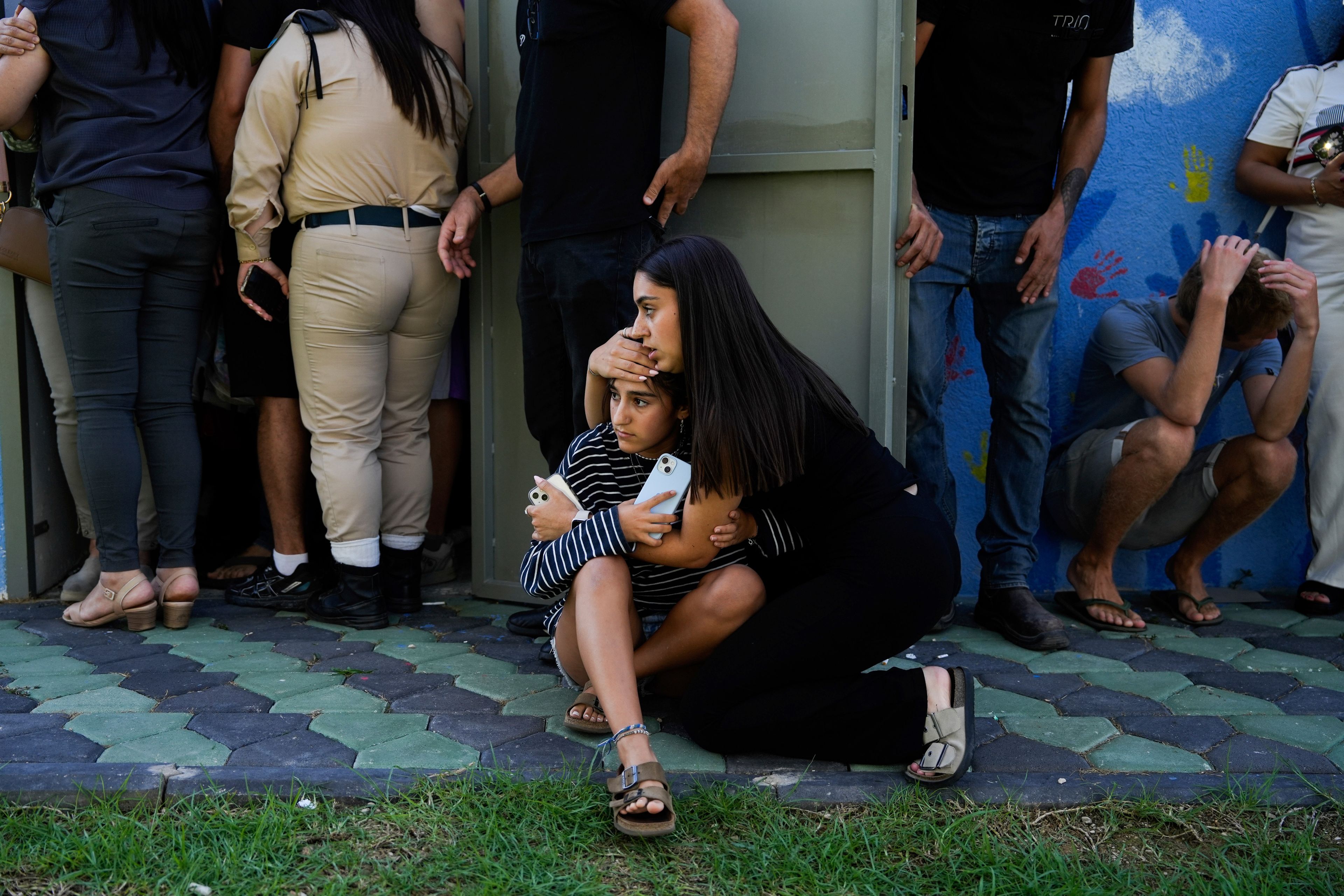 Israelis take cover next to a shelter as a siren sounds a warning of incoming rockets fired from Lebanon, in Nahariya, northern Israel, Thursday, Sept. 19, 2024. (AP Photo/Baz Ratner)