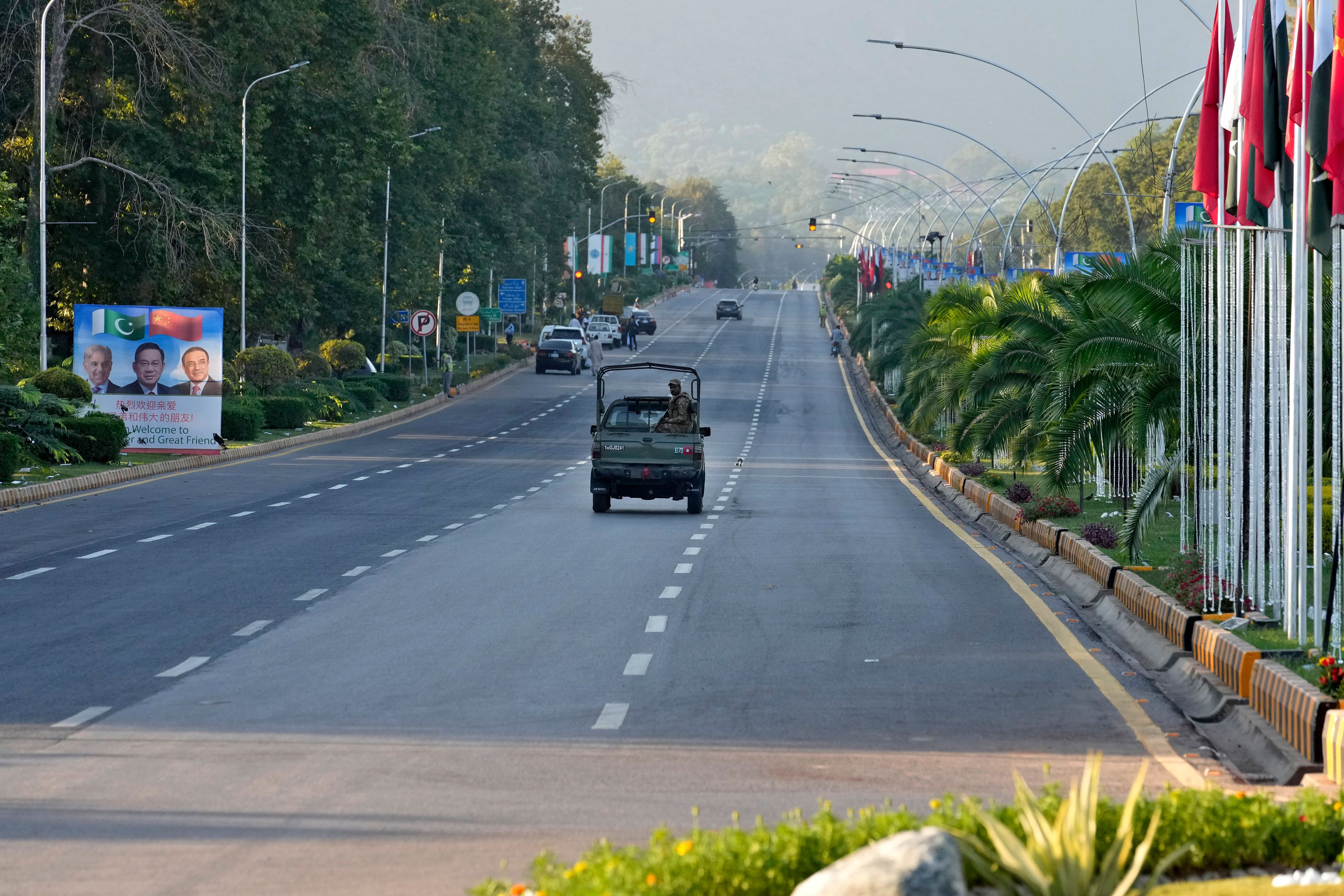 An army vehicle moves past a welcoming billboard with portraits of China's Premier Li Qiang, center, Pakistan's Prime Minister Shehbaz Sharif and President Asif Ali Zardari, displayed along a road leading to the venue of the upcoming Shanghai Cooperation Organization (SCO) summit in Islamabad, Pakistan, Sunday, Oct. 13, 2024. (AP Photo/Anjum Naveed)