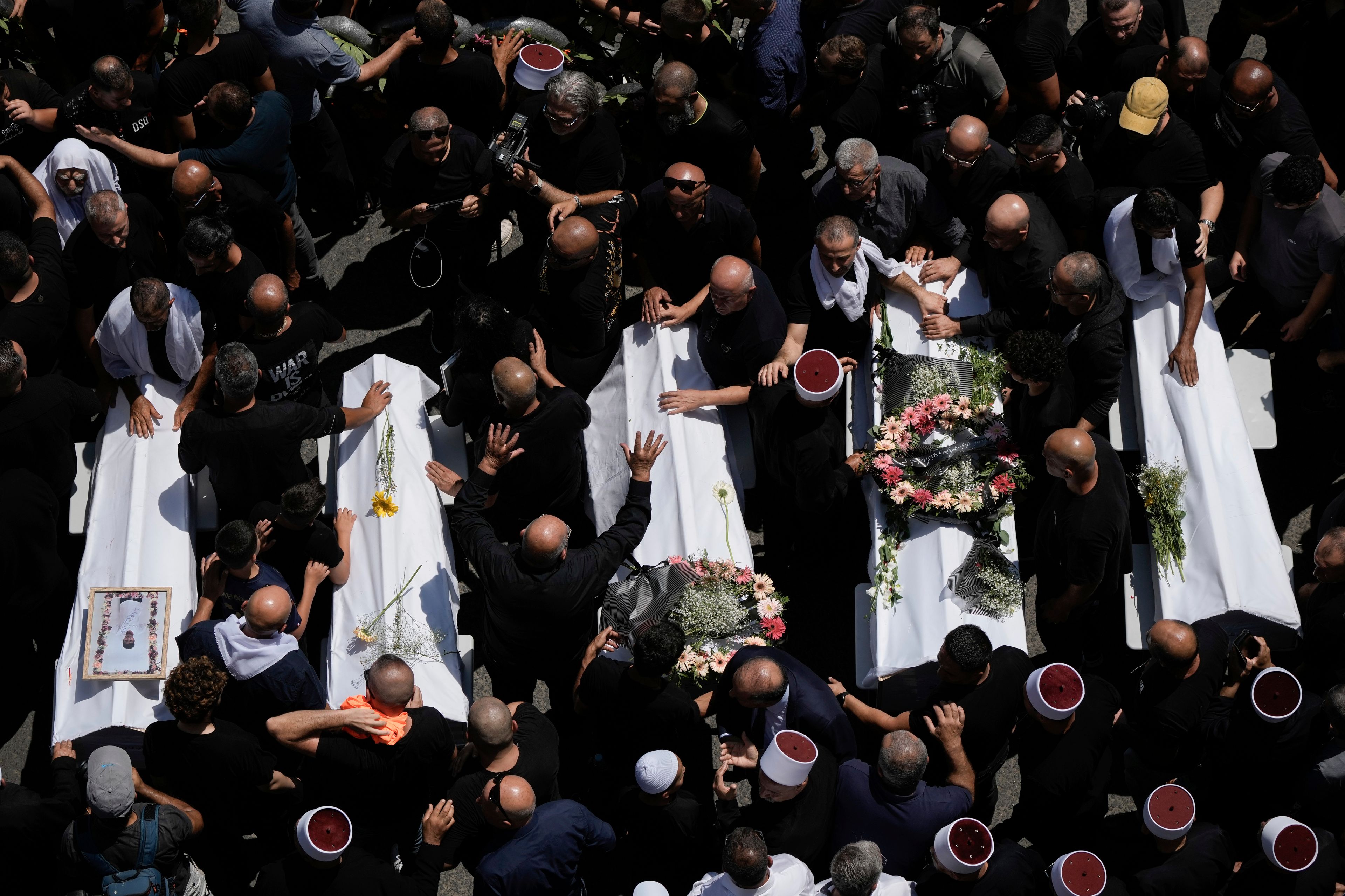 Mourners from the Druze minority surround the bodies of some of the 12 children and teens killed in a rocket strike at a soccer field, in the village of Majdal Shams at the Israeli-controlled Golan Heights, Sunday, July 28, 2024. A rocket strike at a soccer field in the village has killed at least 12 children and teens. It's the deadliest strike on an Israeli target along the country's northern border since the fighting between Israel and the Lebanese militant group Hezbollah began. (AP Photo/Leo Correa)