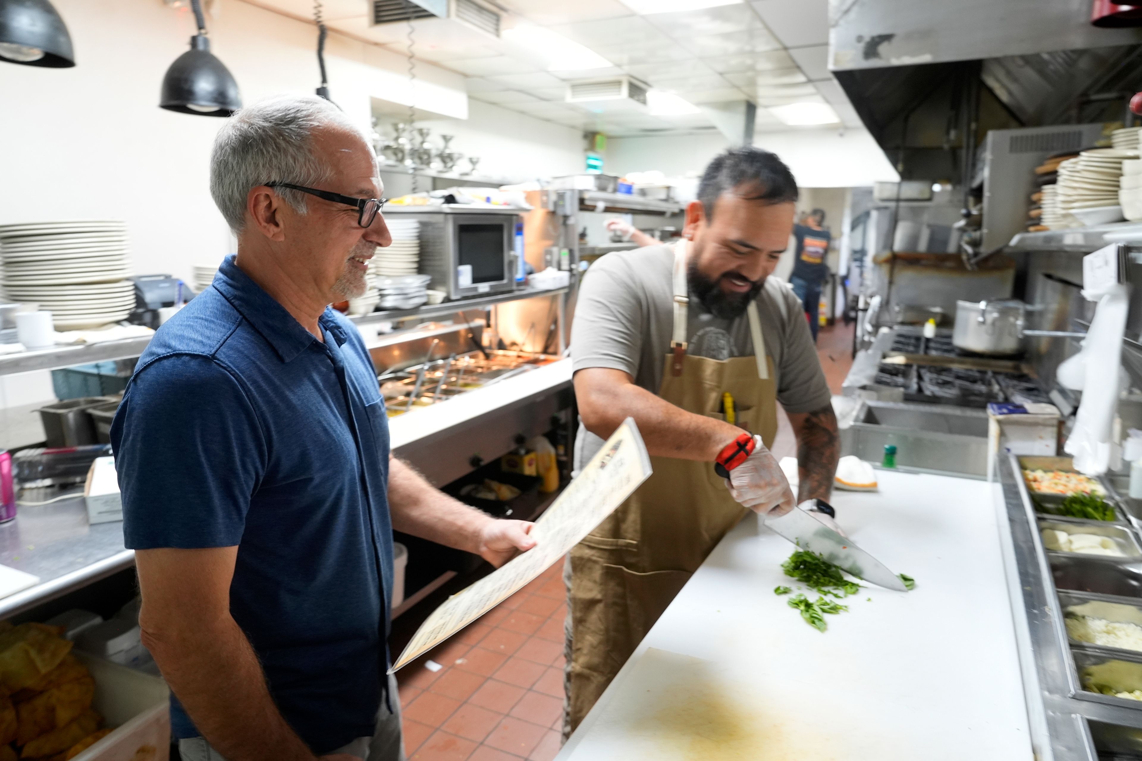 Dan Piacquadio, left, owner of Harold's Cave Creek Corral, waits to talk with chef and kitchen manager Lucio Osorno as he works in the kitchen as Piacquadio waits for the upcoming election and the results of Arizona Prop 138 on minimum wage Thursday, Oct. 3, 2024, in Cave Creek, Ariz. (AP Photo/Ross D. Franklin)