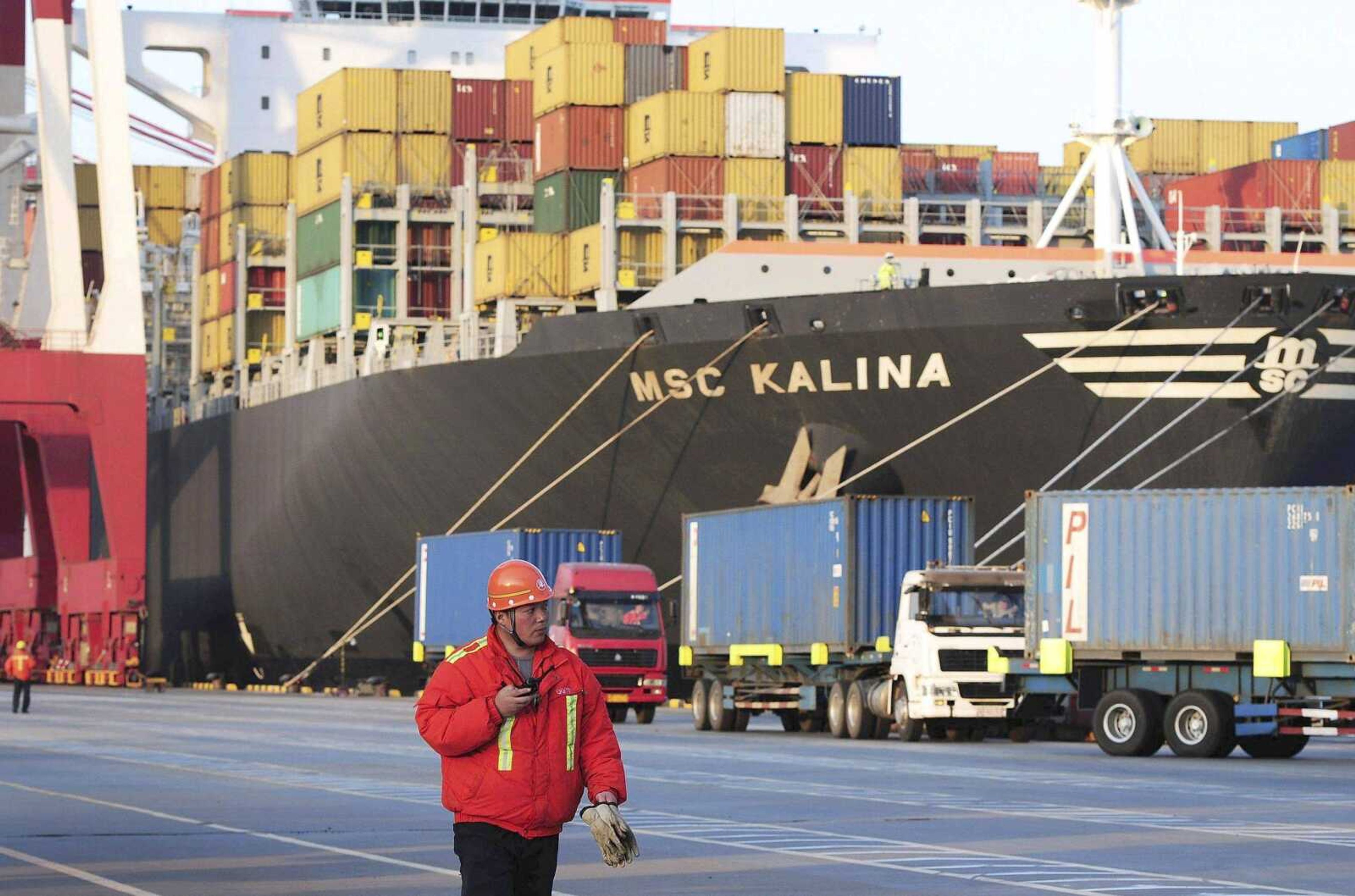 A worker walks past a container vessel docked in Qingdao port April 8 in east China&#8217;s Shandong province. (Associated Press file)