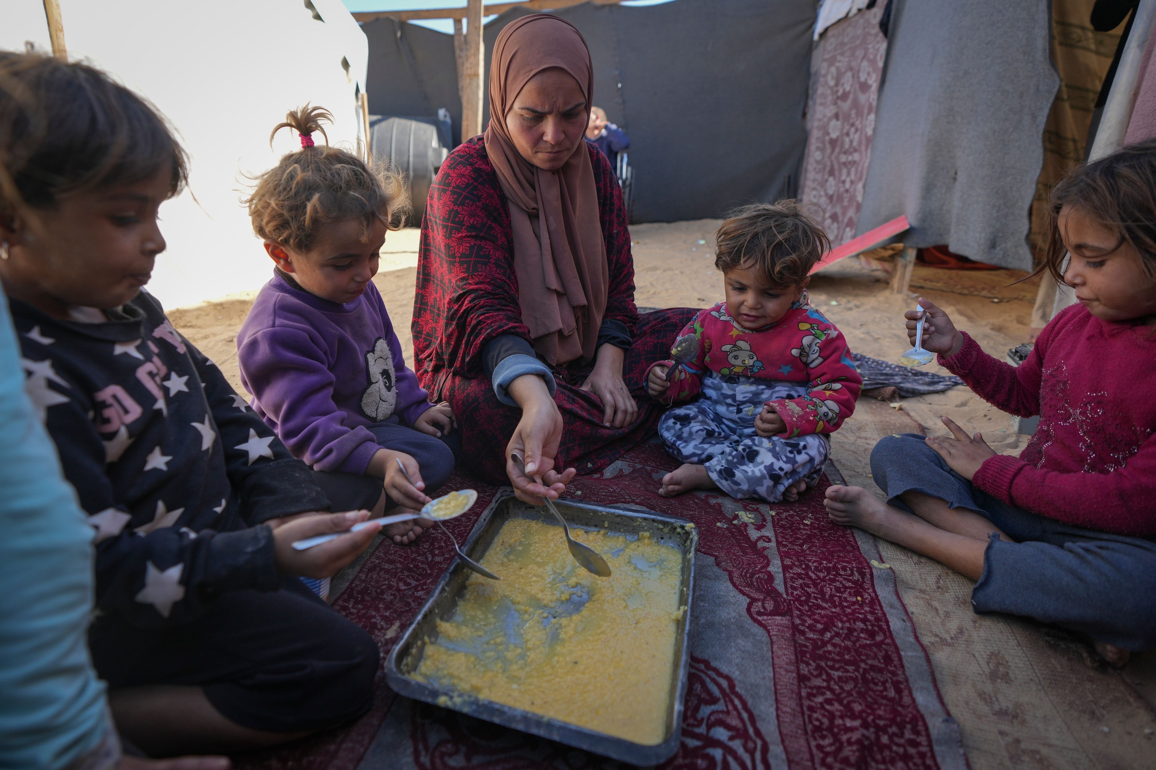 Yasmin Eid and her four daughters eat lentils at their tent in a refugee camp in Deir al-Balah, Gaza Strip, Tuesday Nov. 19, 2024. (AP Photo/Abdel Kareem Hana)