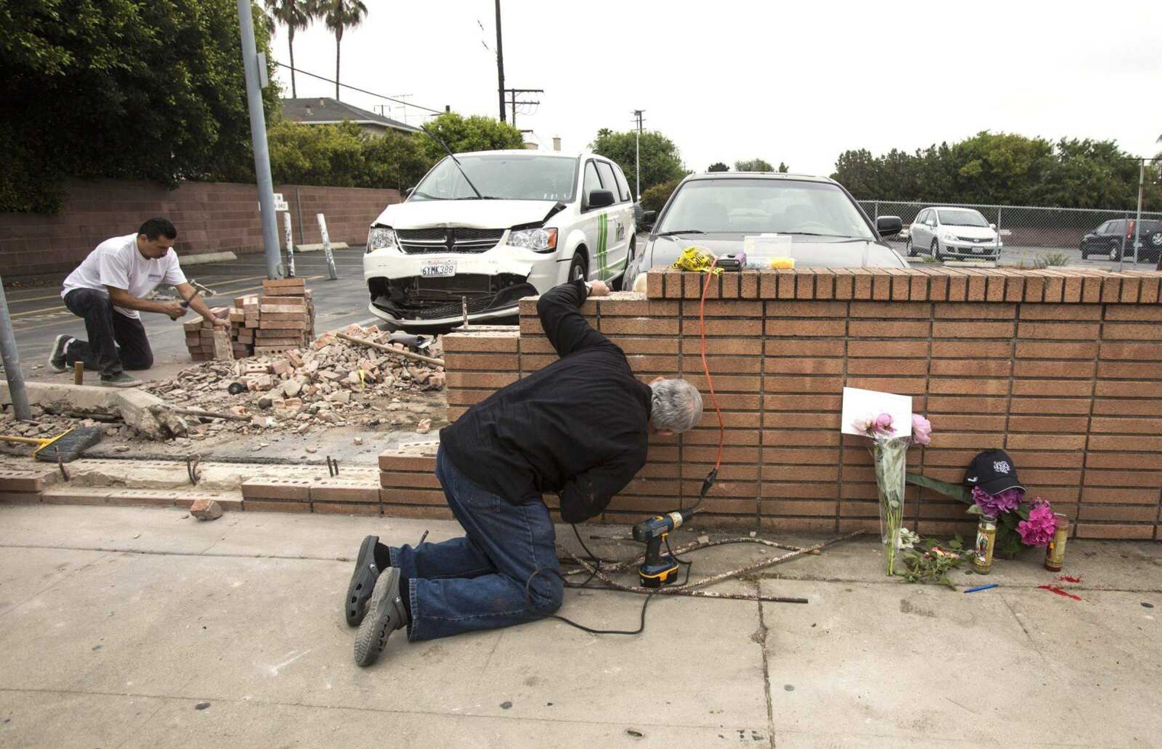 Akiva Sherman, right, 62, repairs the wall next to a makeshift memorial Sunday where a victim&#8217;s vehicle crashed during the shootings at Santa Monica College in Santa Monica, Calif. (Ringo H.W. Chiu ~ Associated Press)