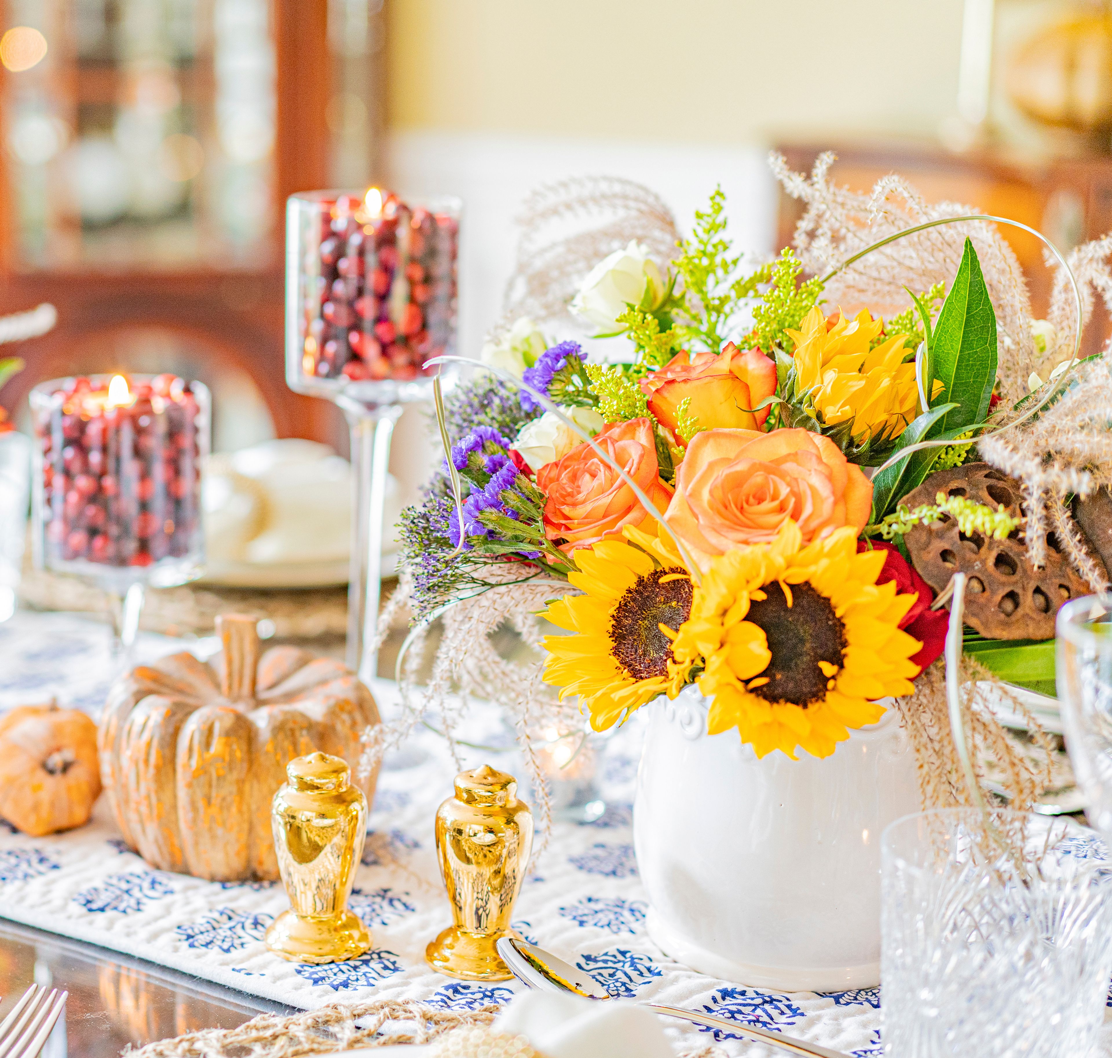 This image provided by Jessie-Sierra Ross shows a colorful Thanksgiving harvest tablescape using fall colors and tall glass candlesticks. Ross, an entertaining and food blogger, filled the candlesticks with fresh cranberries and tea lights for a creative lighting idea. Supermarket flowers and simple candles are really all you need to create ambience at a dinner party. (Jonathan Ross/Jessie-Sierra Ross via AP)