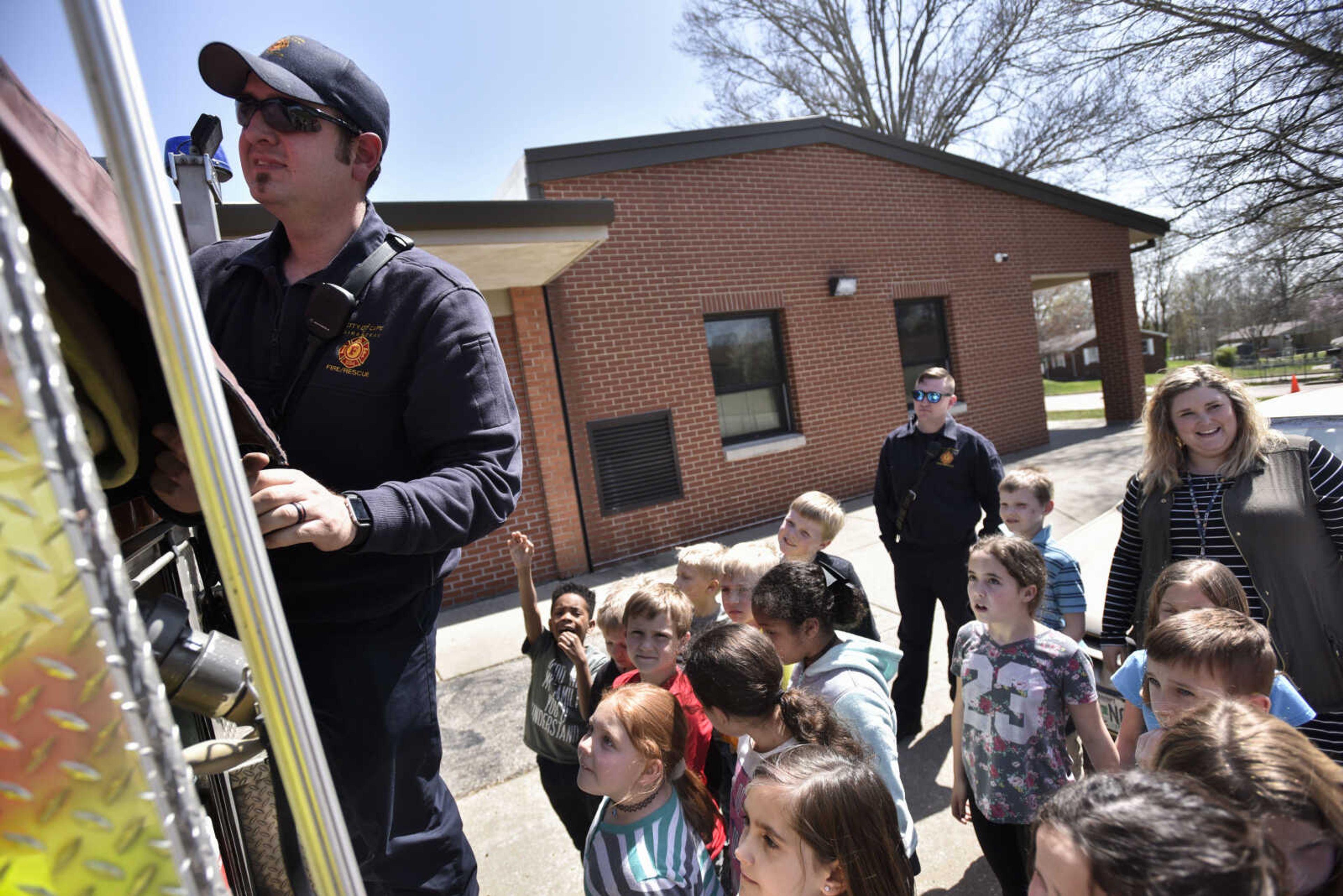 Cape Girardeau firefighter Justin Siemers removes a cover from the back of a firetruck while giving second grade Alma Schrader Elementary students a tour Tuesday, April 17, 2018, in Cape Girardeau.