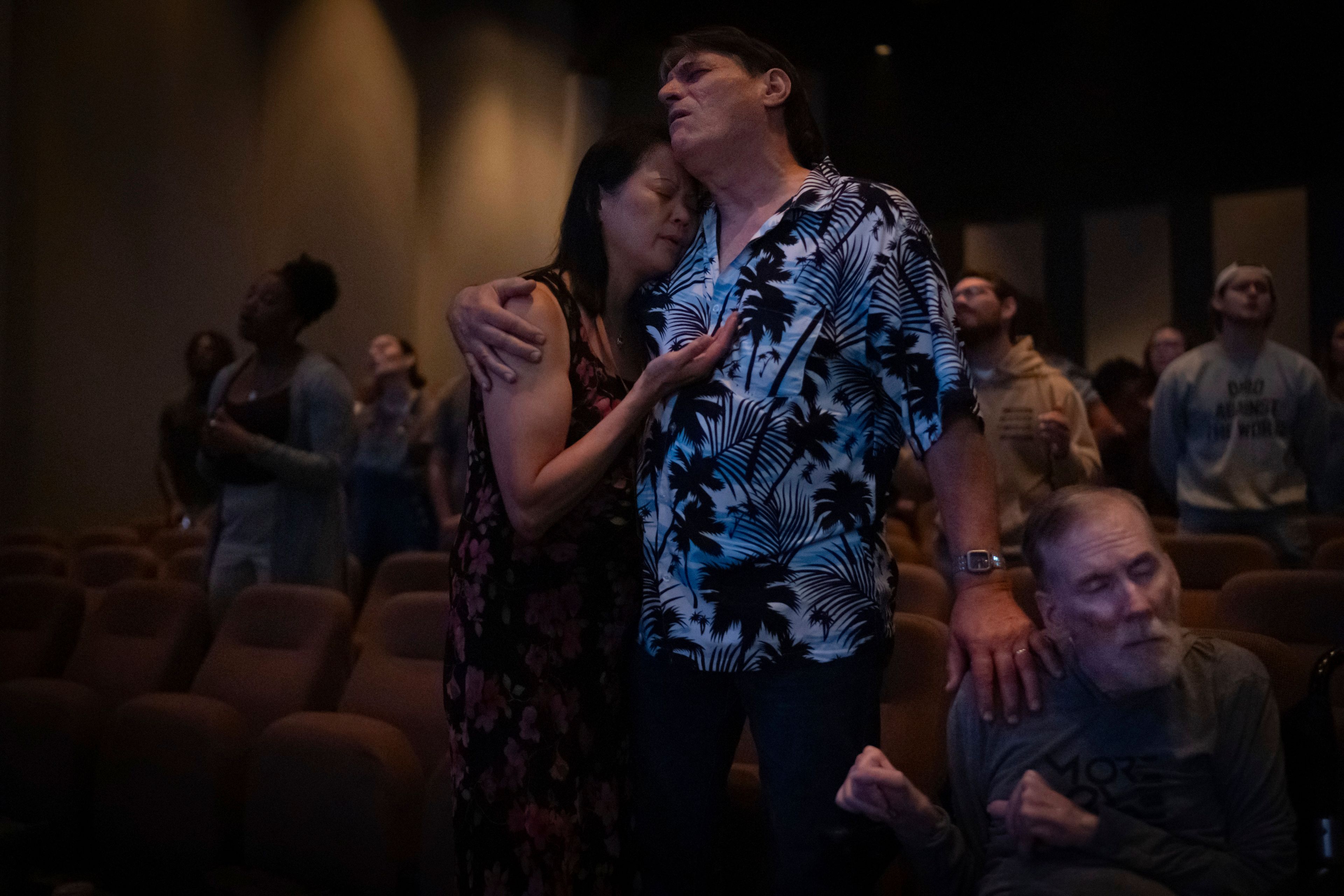 Lesley Dzik, left, and her husband, Matt, embrace each other while praying with Richard Wellbank at The Vineyard Church in Urbana, Ill., Sunday, Sept. 22, 2024. Lesley, a Republican, and Matt, a Democrat, have navigated issues common to so many marriages, from parenting to money. But politics? That's complicated. (AP Photo/David Goldman)